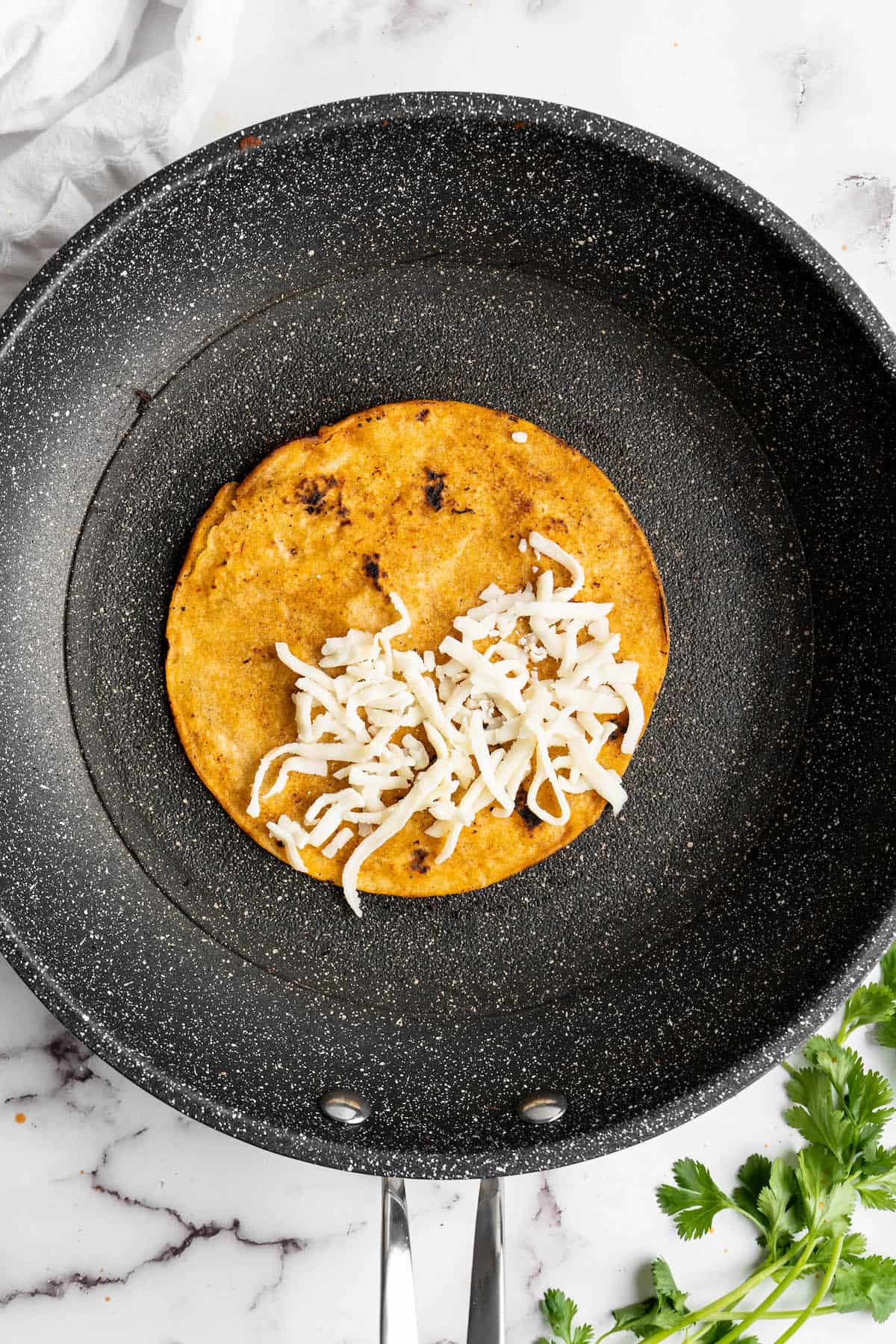 Overhead view of tortilla in skillet, topped with vegan cheese