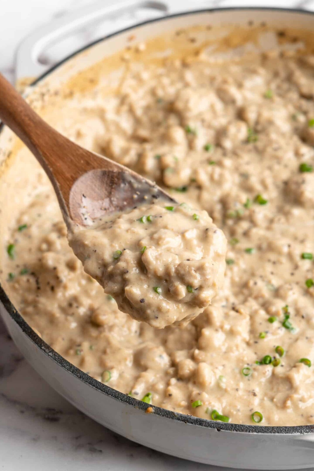 Close up of a wooden spoon with a spoonful of vegan gravy on it, with a pot full of gravy in the background