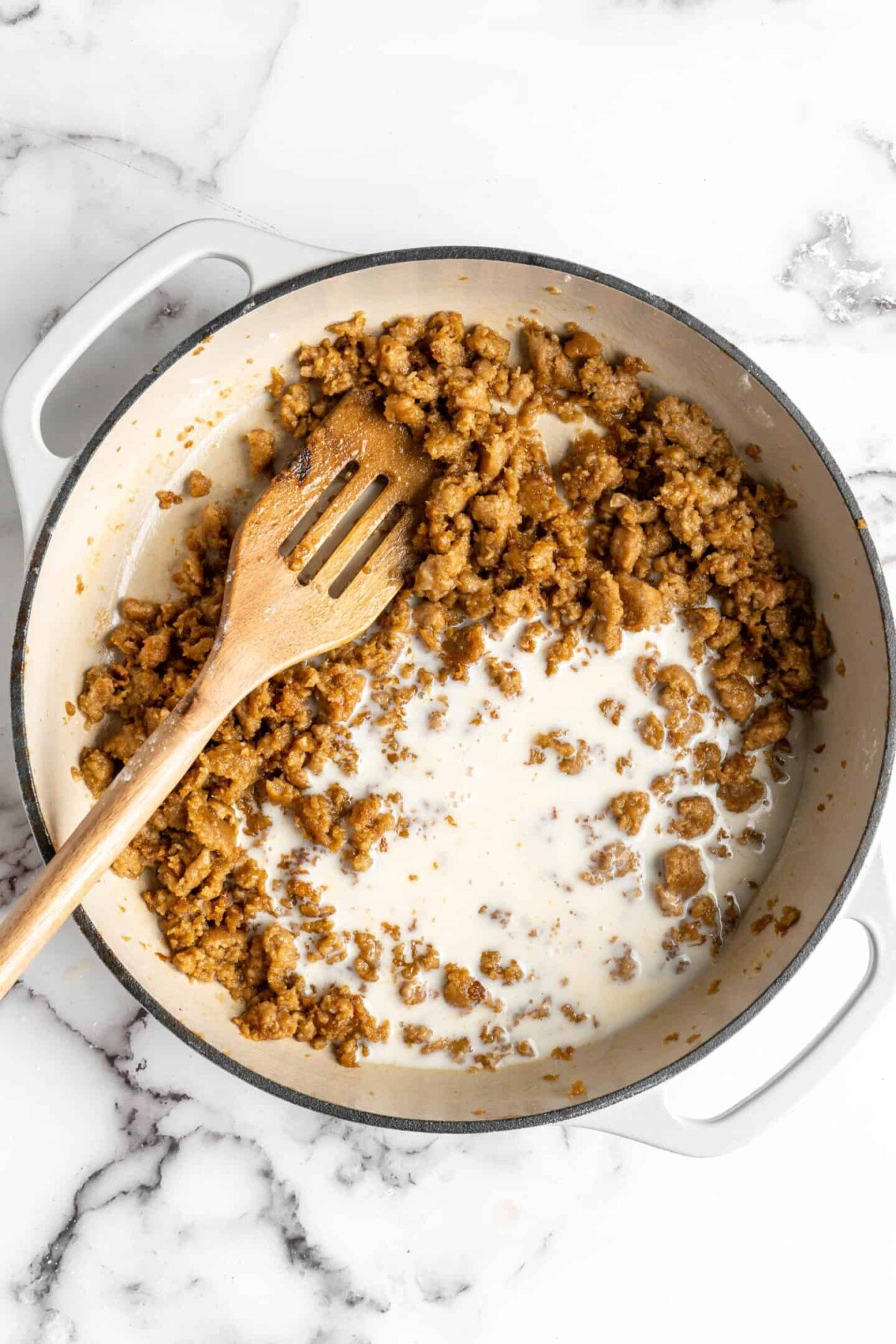 Cooked vegan sausage and a little bit of milk in a dutch oven with a slotted wooden spoon