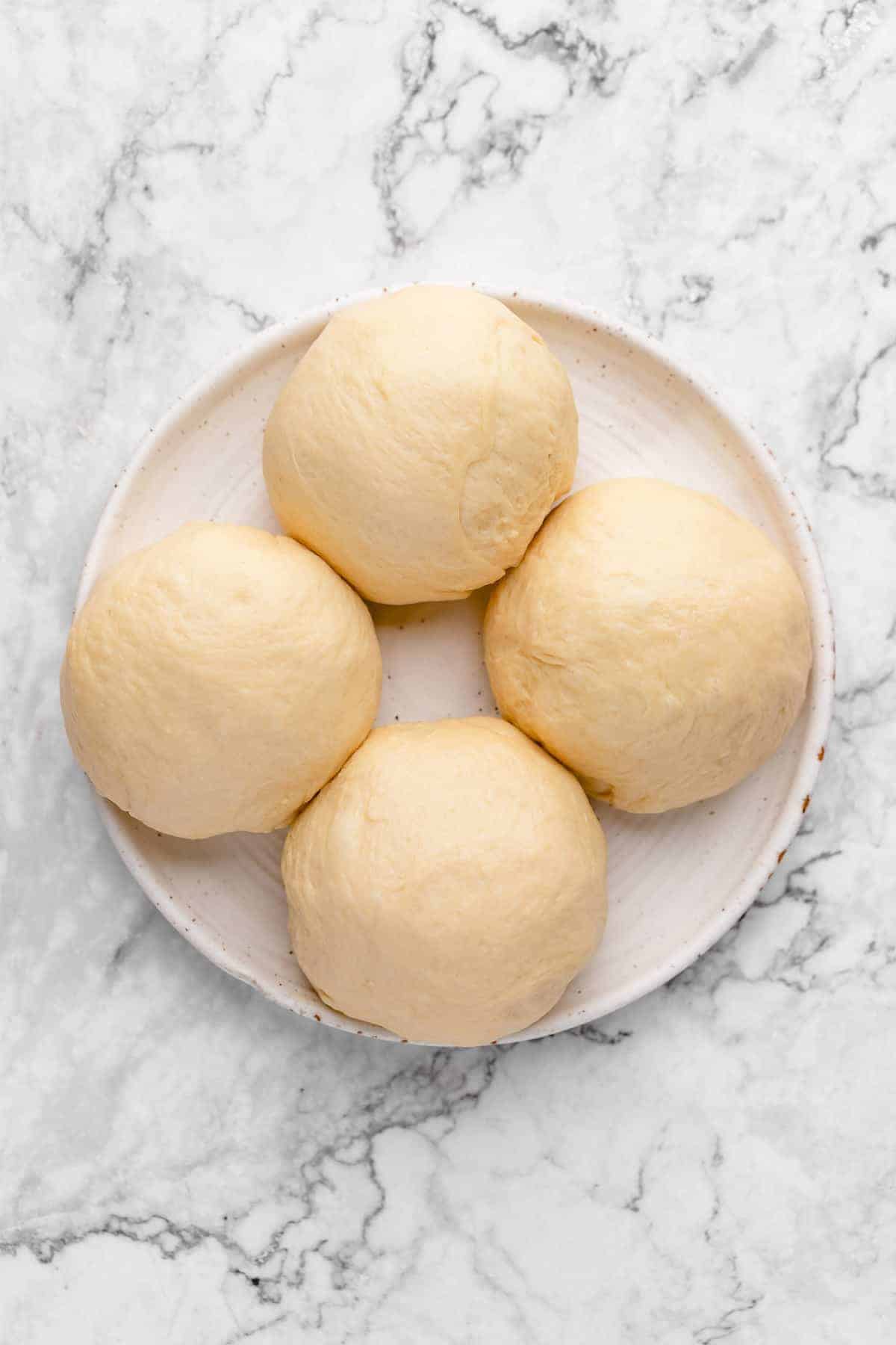 4 balls of Japanese milk bread dough on a plate before baking