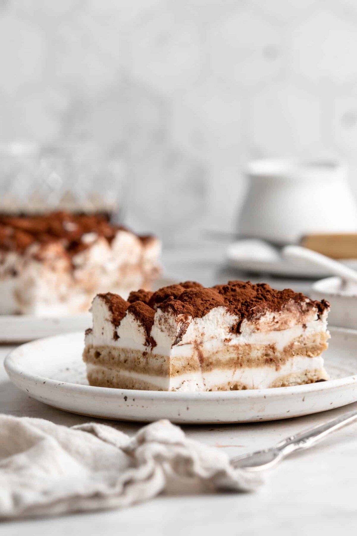 A slice of tiramisu on a plate, with another slice in the background