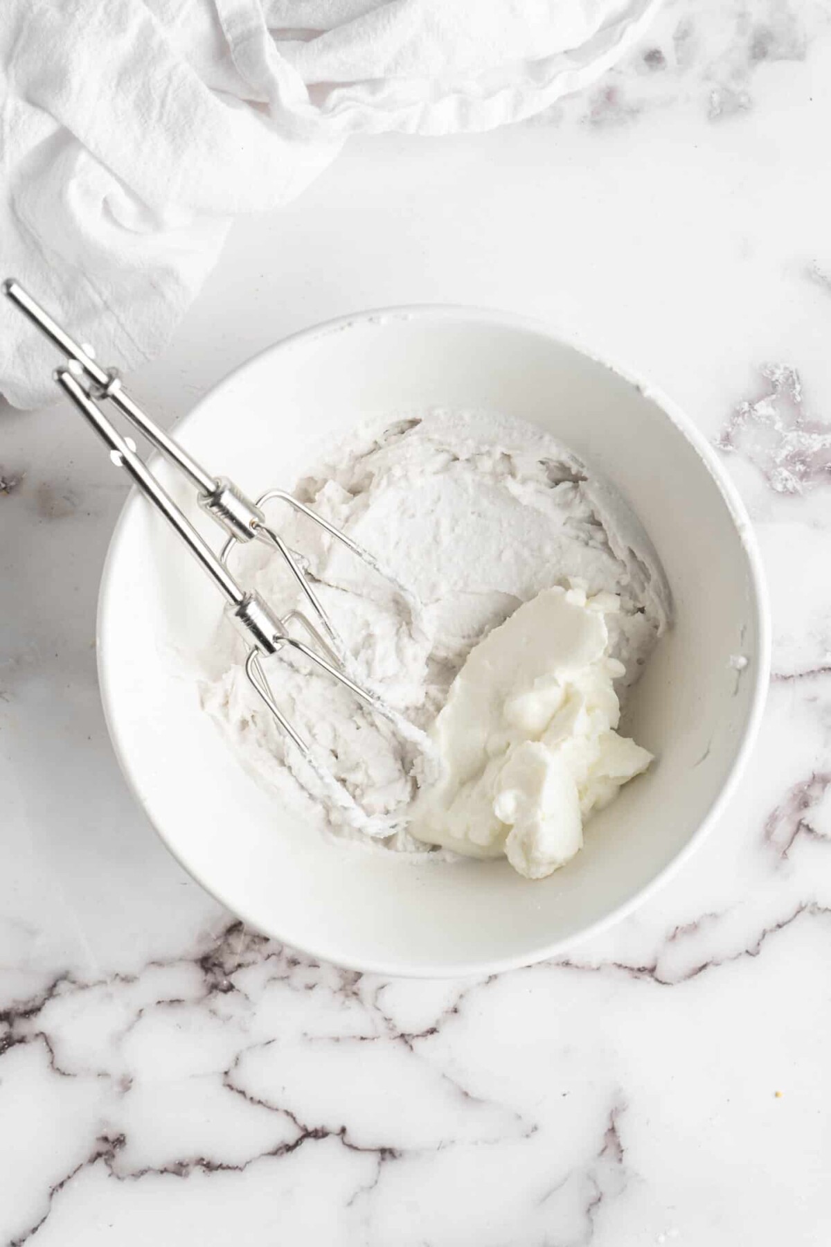 A mixing bowl with whipped coconut milk, vegan yogurt, and two beaters sticking out