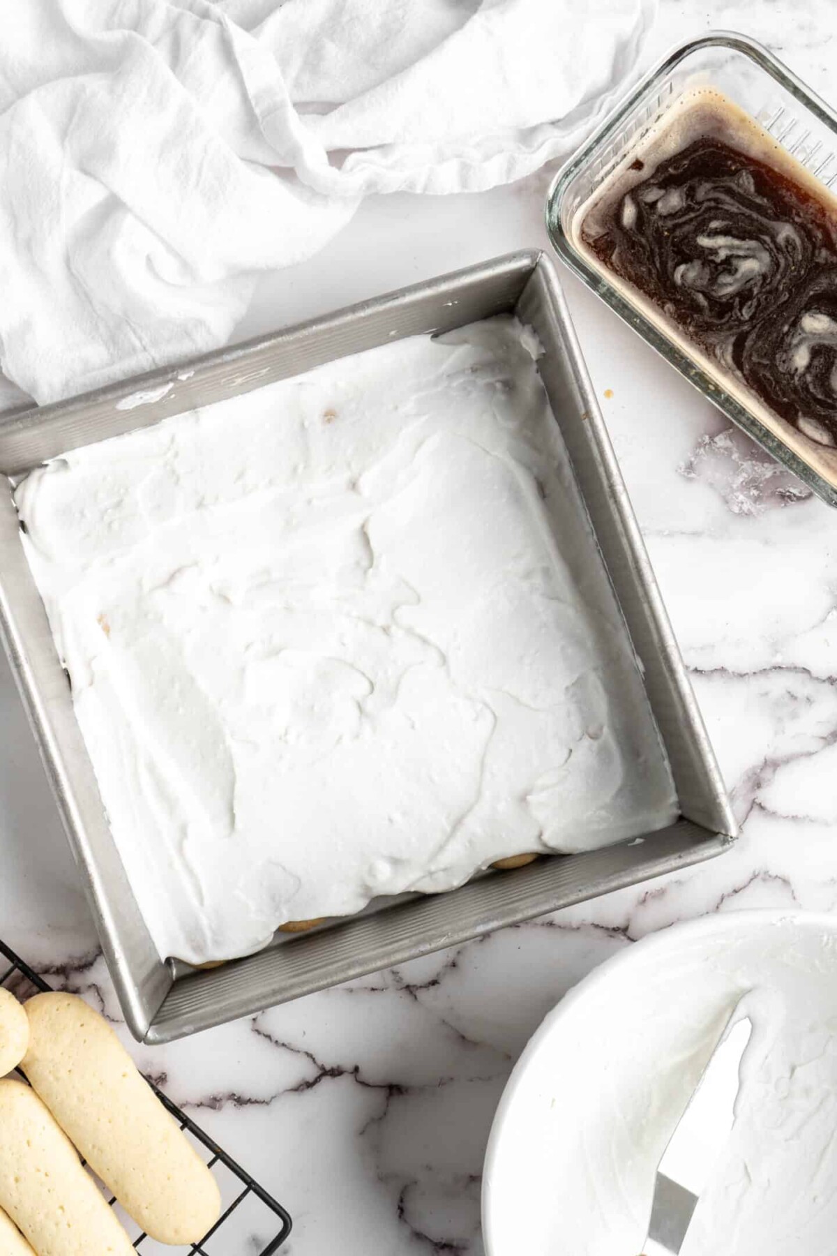 A baking dish with a layer of mascarpone spread over ladyfingers