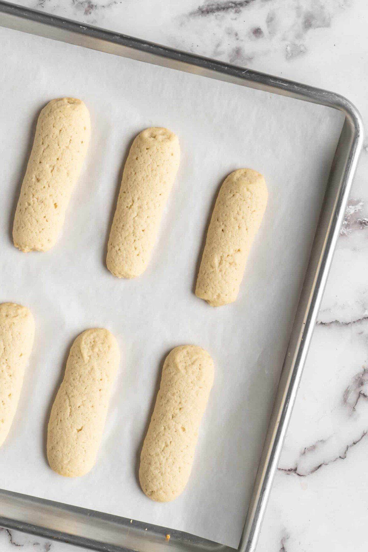 A baking sheet with cooked ladyfinger cookies on parchment paper