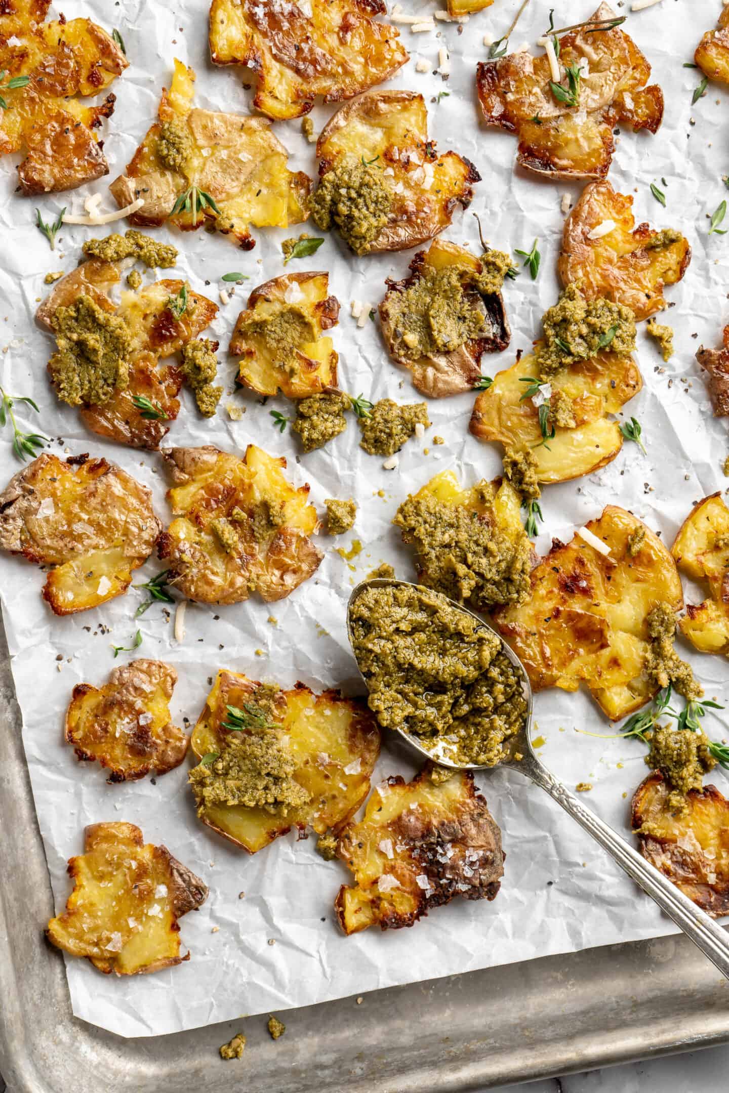 Crispy smashed potatoes on a sheet pan topped with pesto