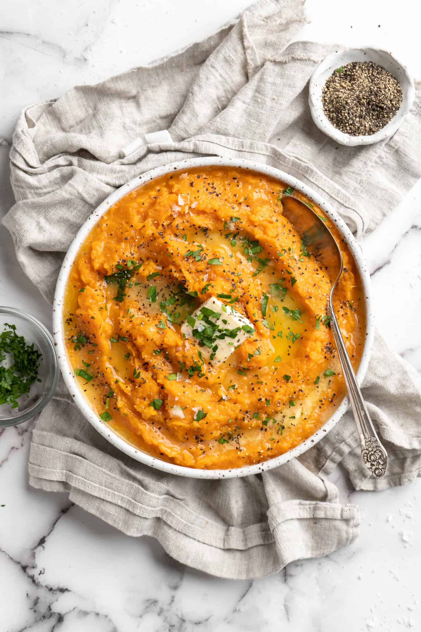 mashed sweet potatoes topped with vegan butter and parsley in a bowl