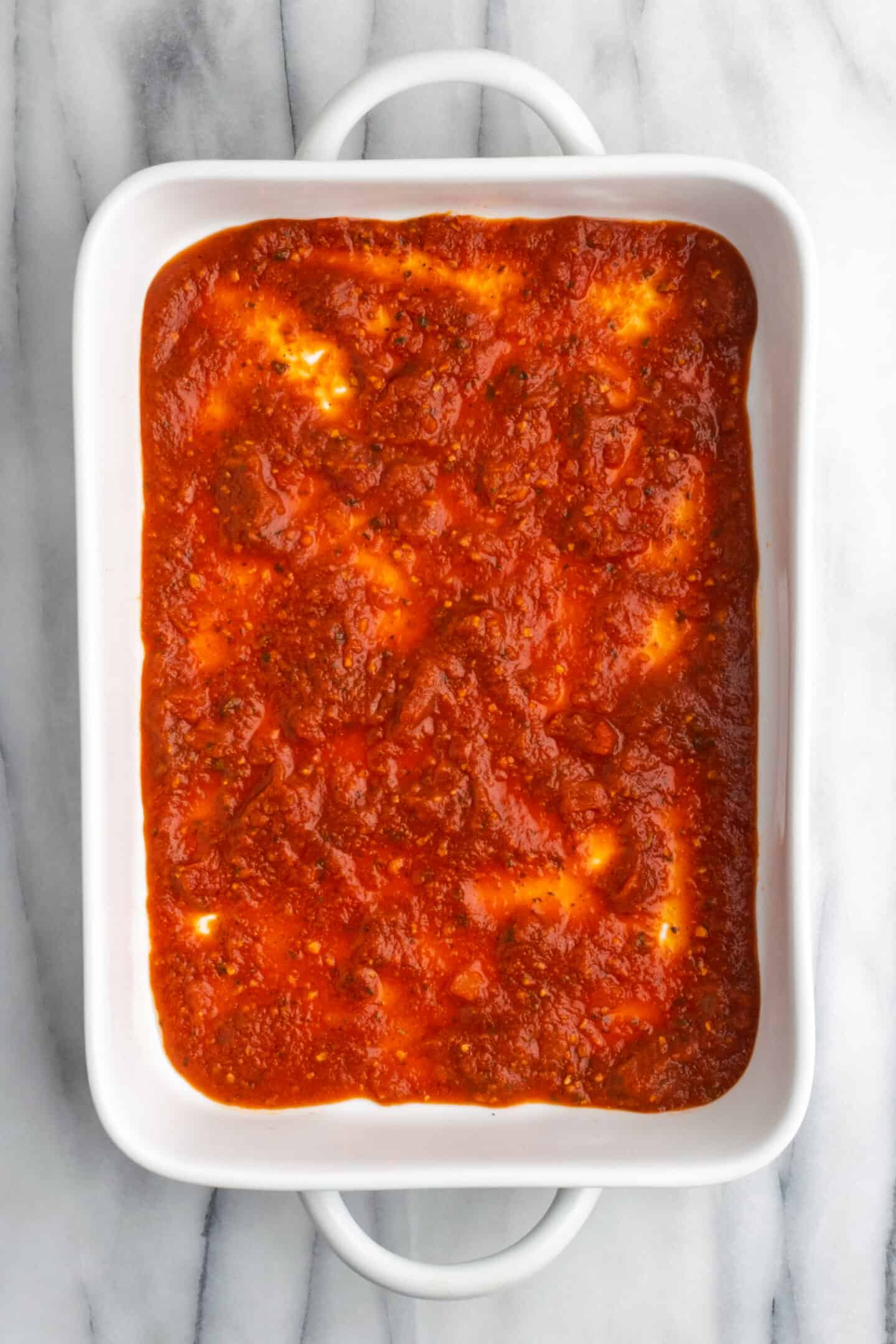 Marinara sauce spread in the bottom of a casserole dish