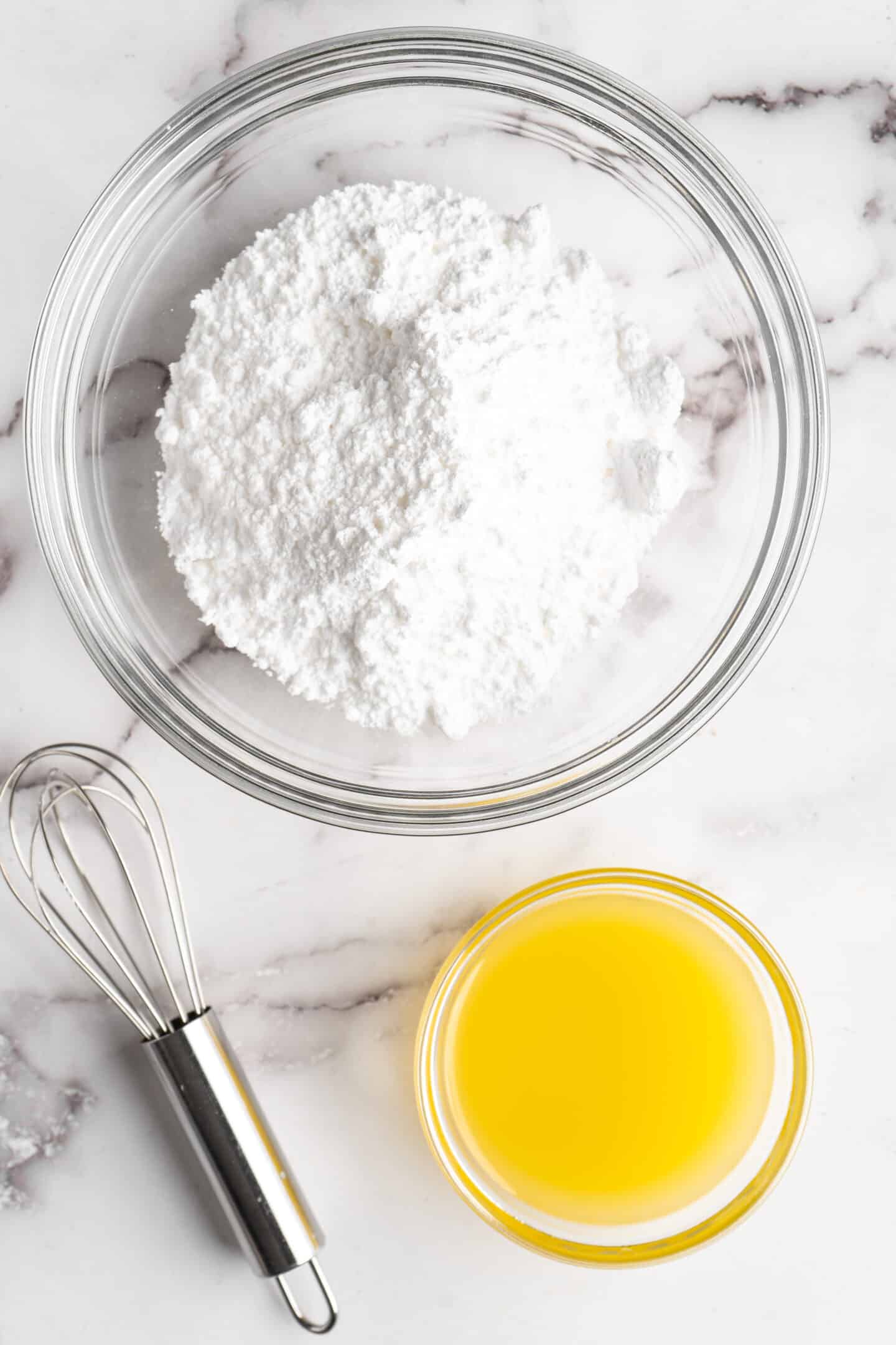 A bowl of powdered sugar next to a bowl of orange juice, with a whisk next to them