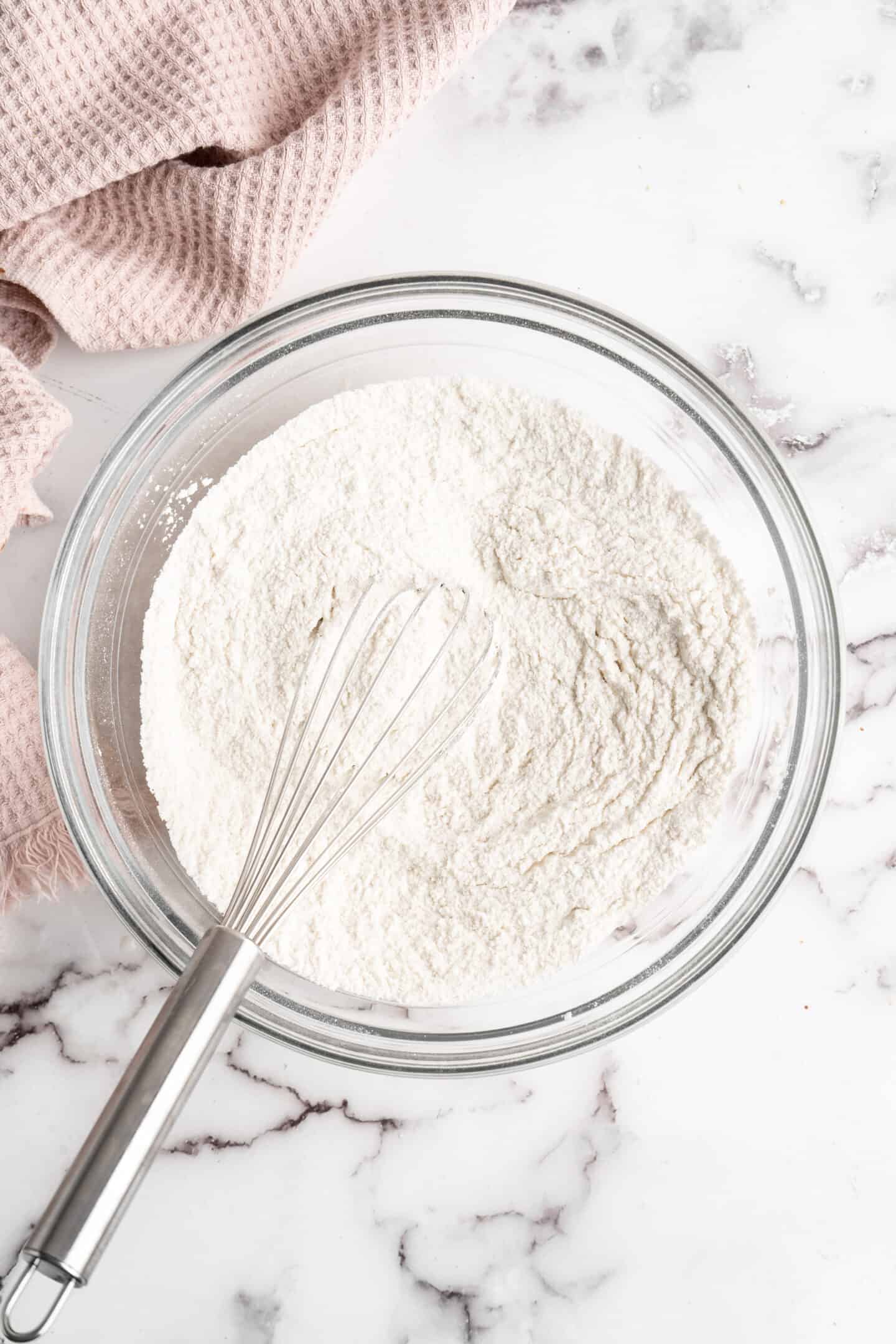 A mixing bowl filled with a flour and sugar mixture, with a whisk in it