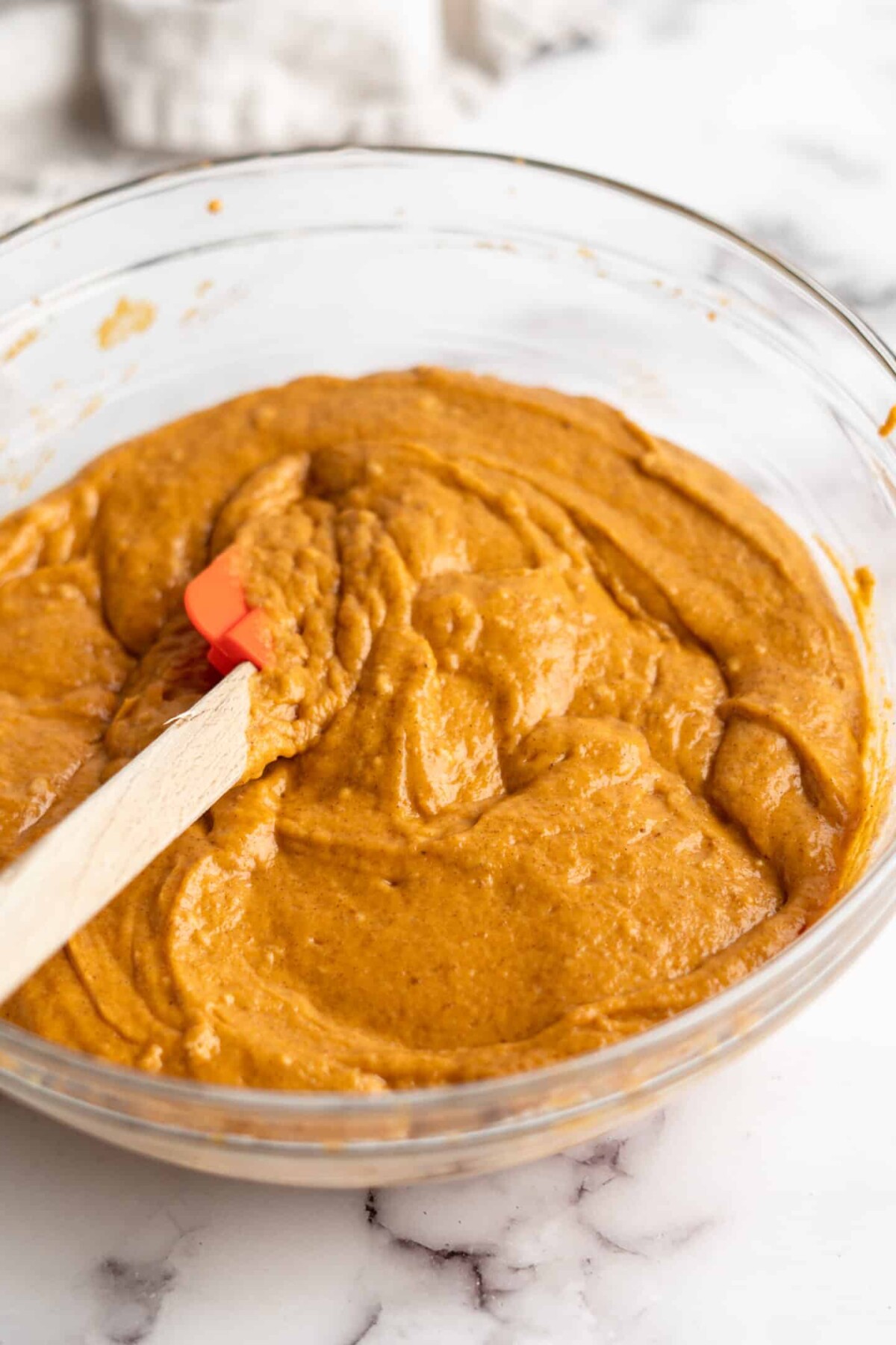 A mixing bowl filled with pumpkin cupcake batter, with a rubber spatula in it.