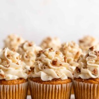 Three pumpkin cupcakes topped with cream cheese and pecans, with three more behind them