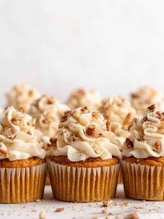 Three pumpkin cupcakes topped with cream cheese and pecans, with three more behind them