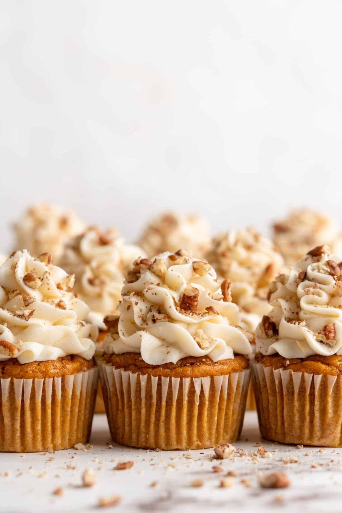 Three pumpkin cupcakes topped with cream cheese and pecans, with three more behind them