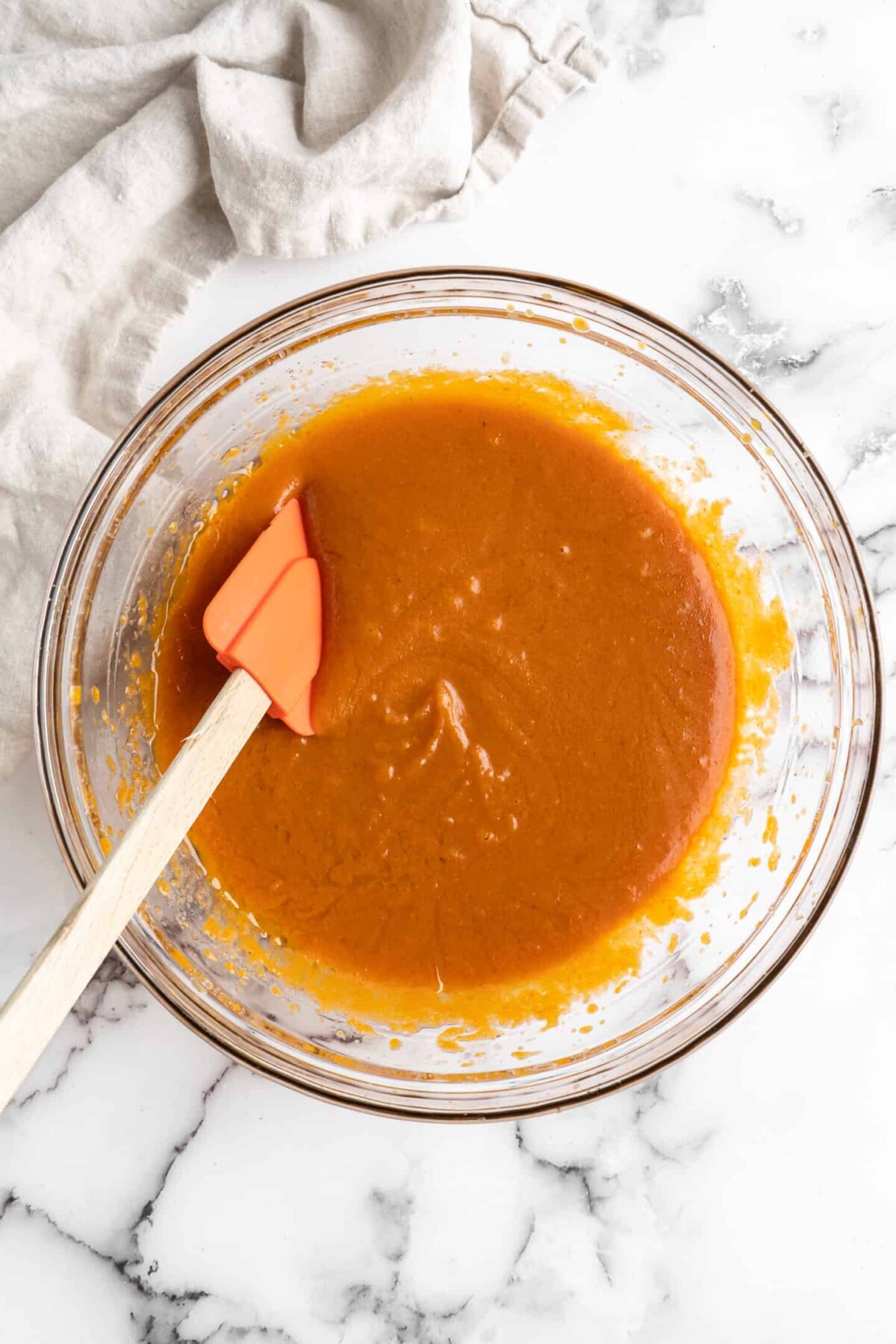 A mixing bowl with pumpkin puree, milk, and sugar mixed together in it, with a rubber spatula.