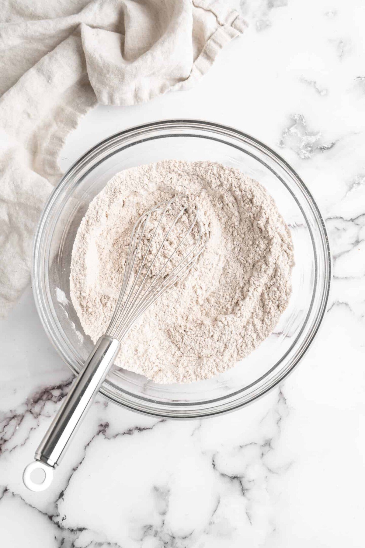 A mixing bowl filled with a flour mixture, with a whisk in it.