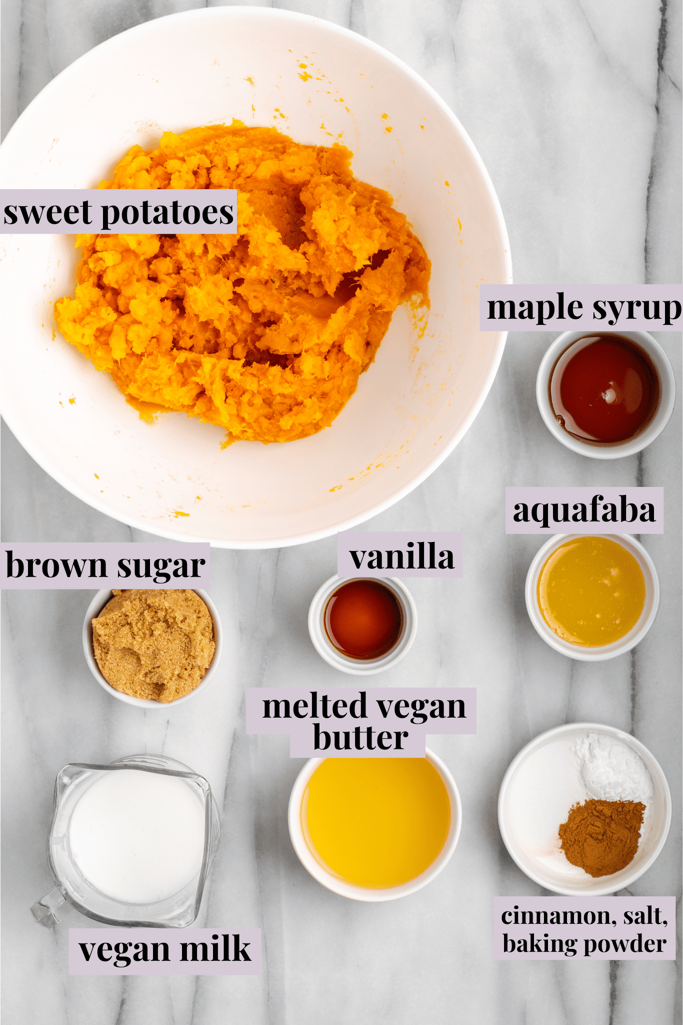 Overhead view of the ingredients for sweet potato soufflé: a bowl of sweet potatoes, a bowl of melted butter, a bowl of non-dairy milk, a bowl of vanilla extract, a bowl of aquafaba, a bowl of brown sugar, and a bowl of salt, cinnamon, and baking powder