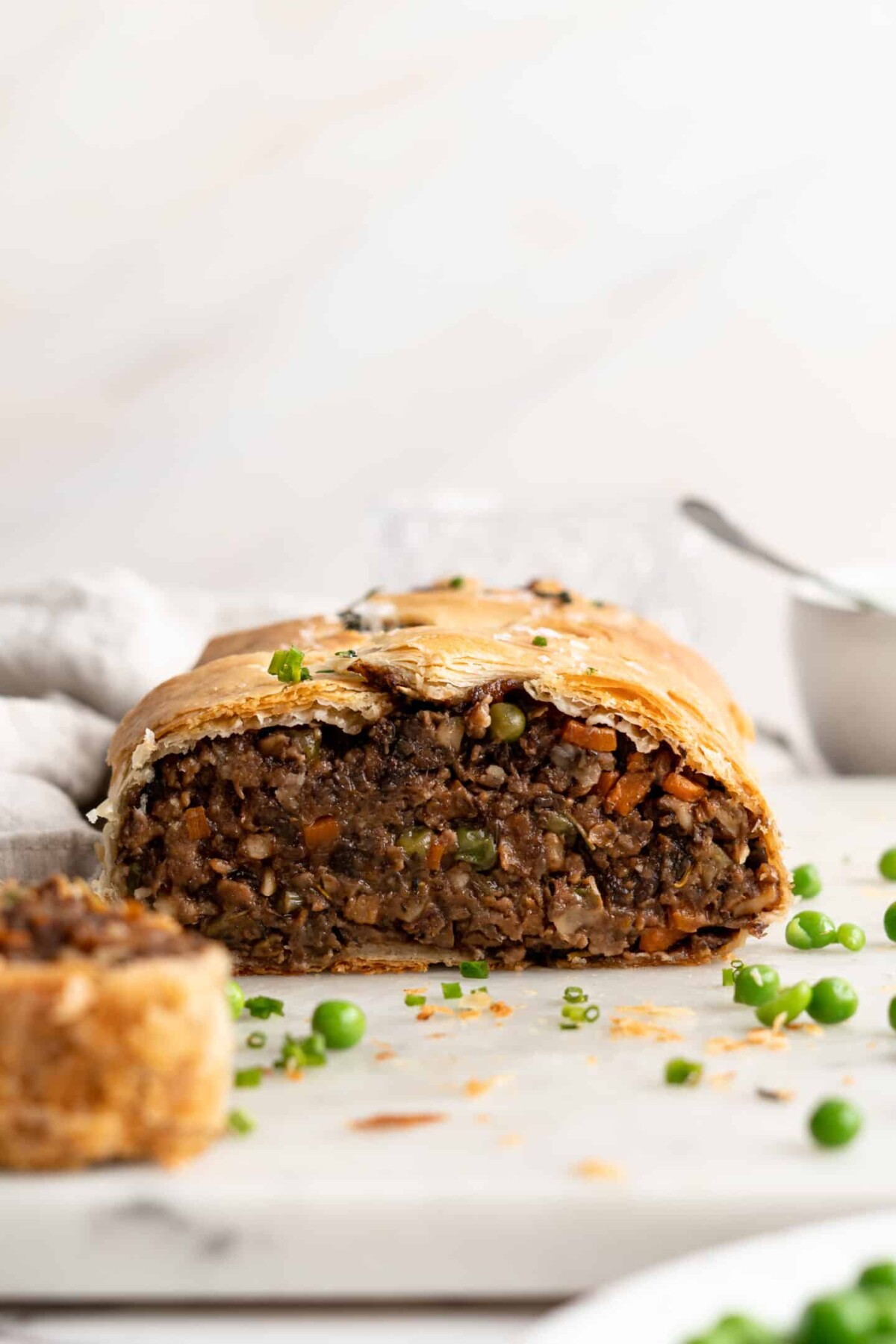 Front on view of a vegan wellington that's been cut in half, surrounded by peas