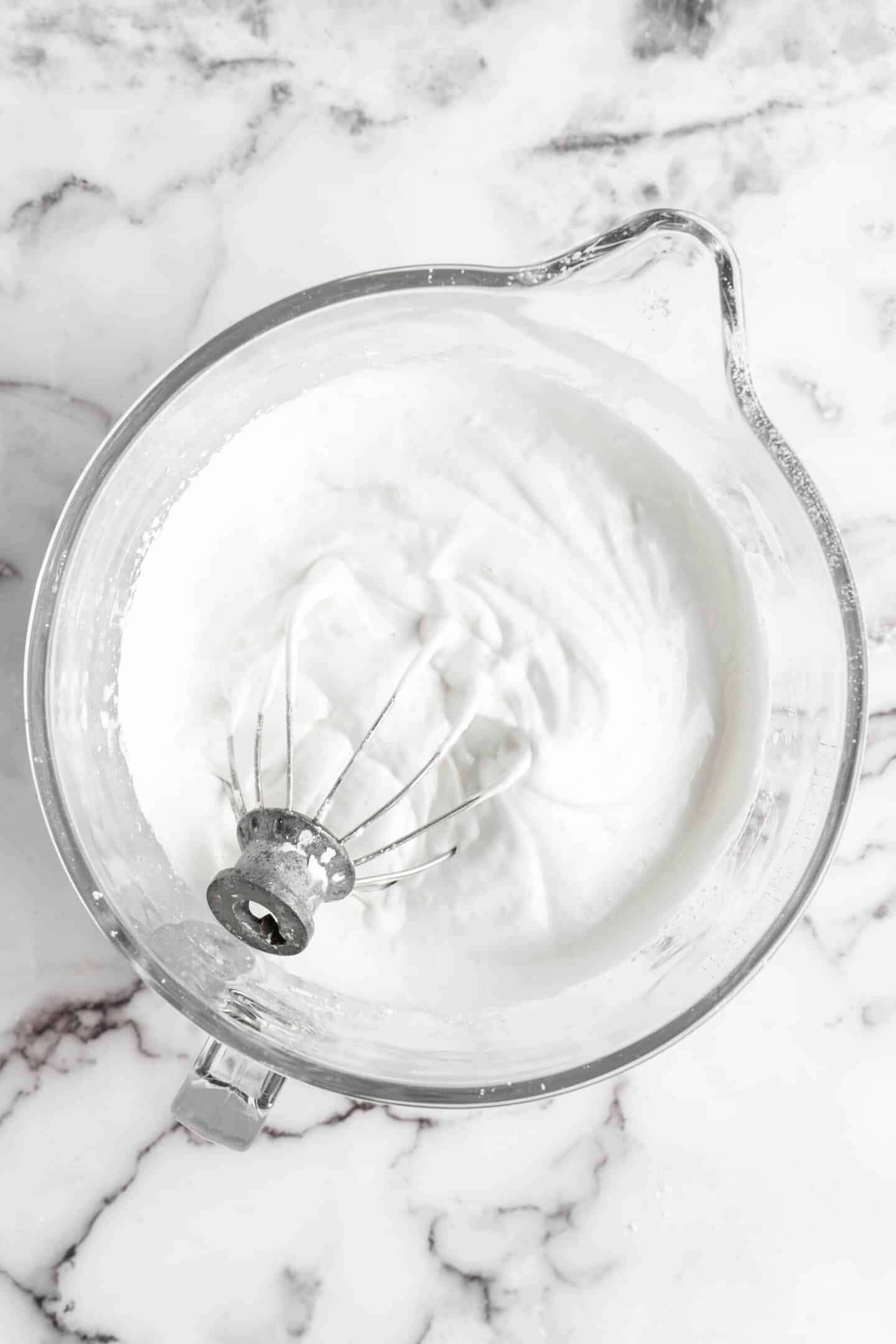 whipped aquafaba in a glass bowl with a wire whip in it