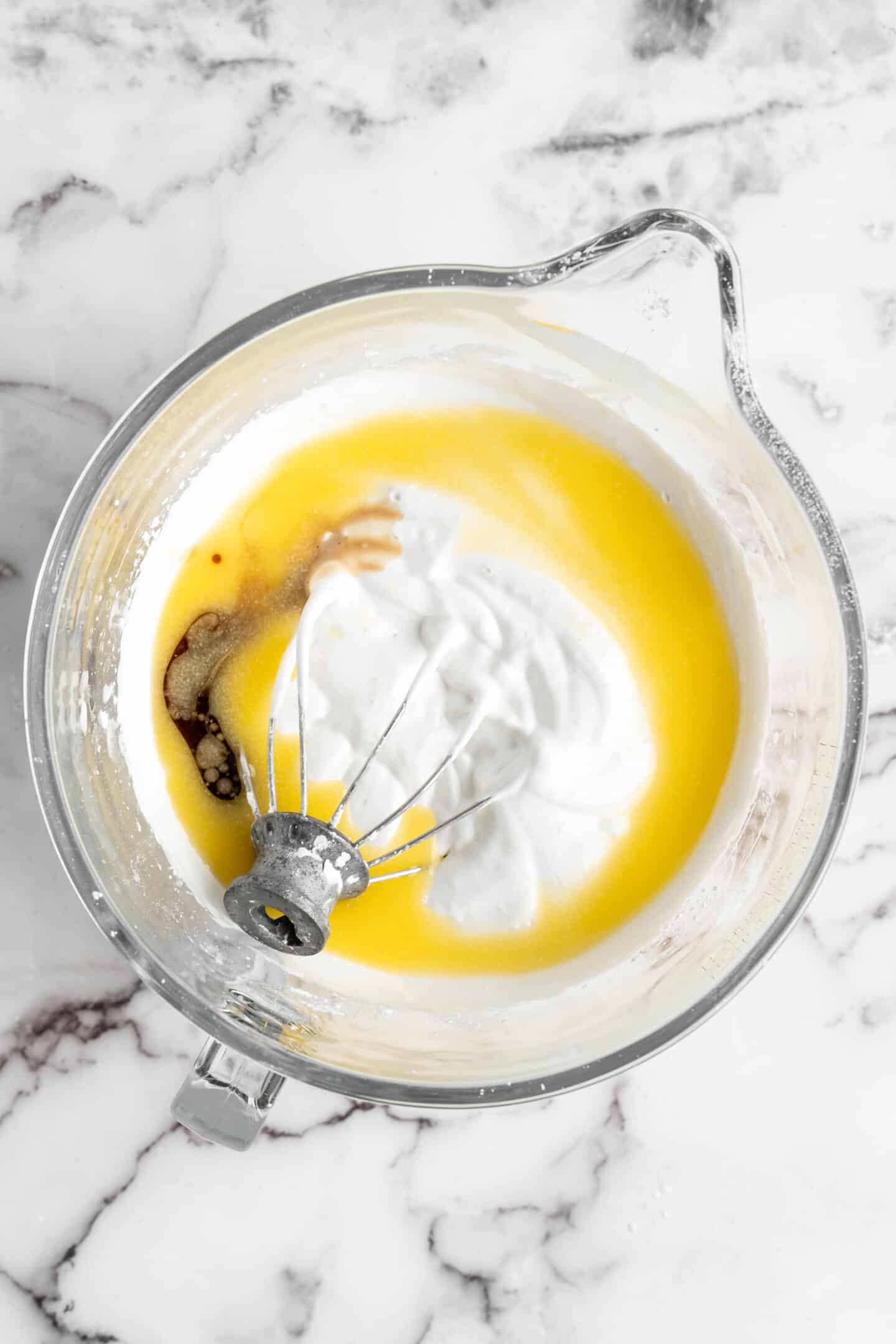 a glass bowl with vanilla, vegan butter and whipped aquafaba in it with a wire whip attachment