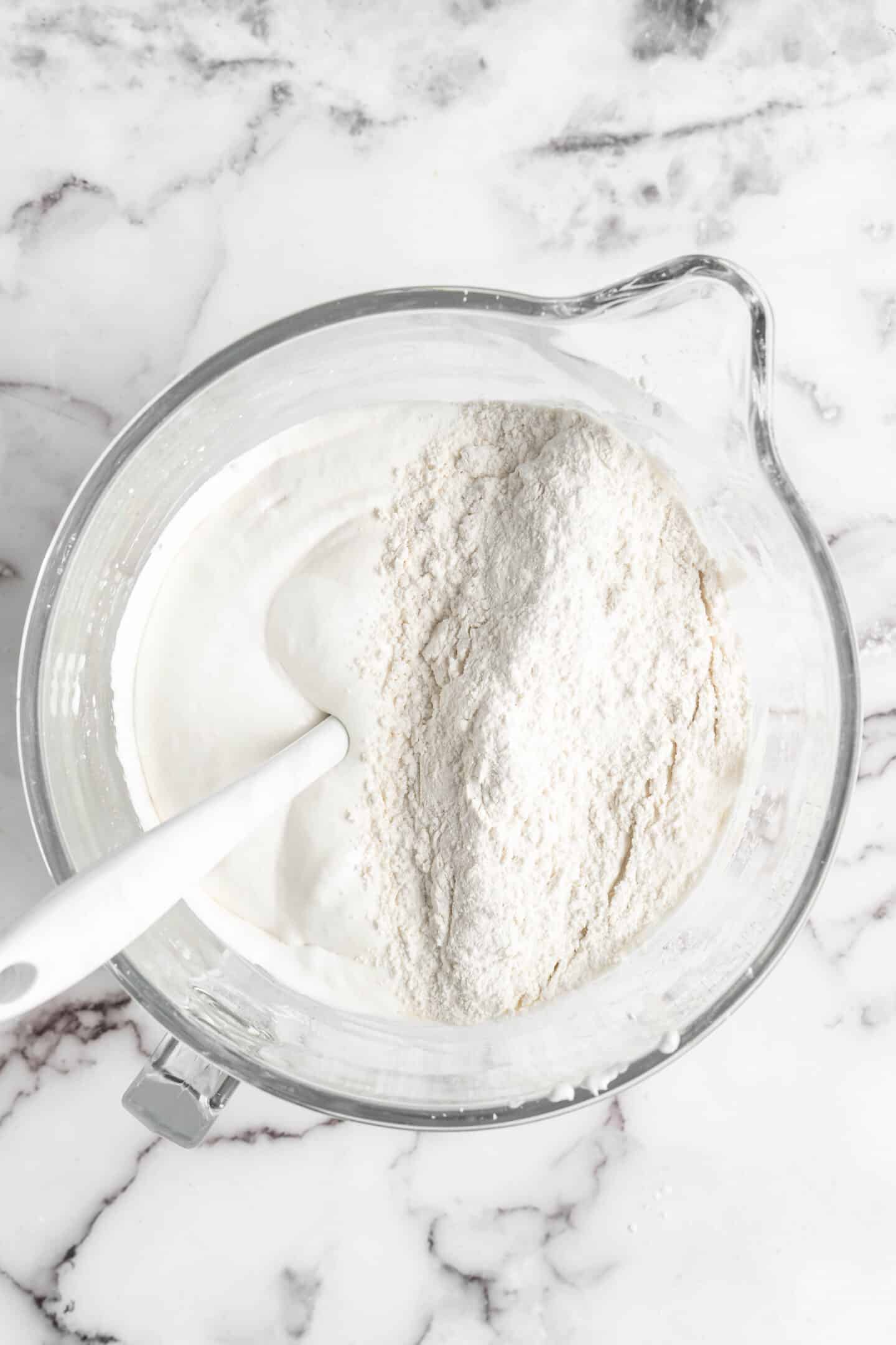 whisked flour on top of whipped aquafaba mix with a white spatula in it