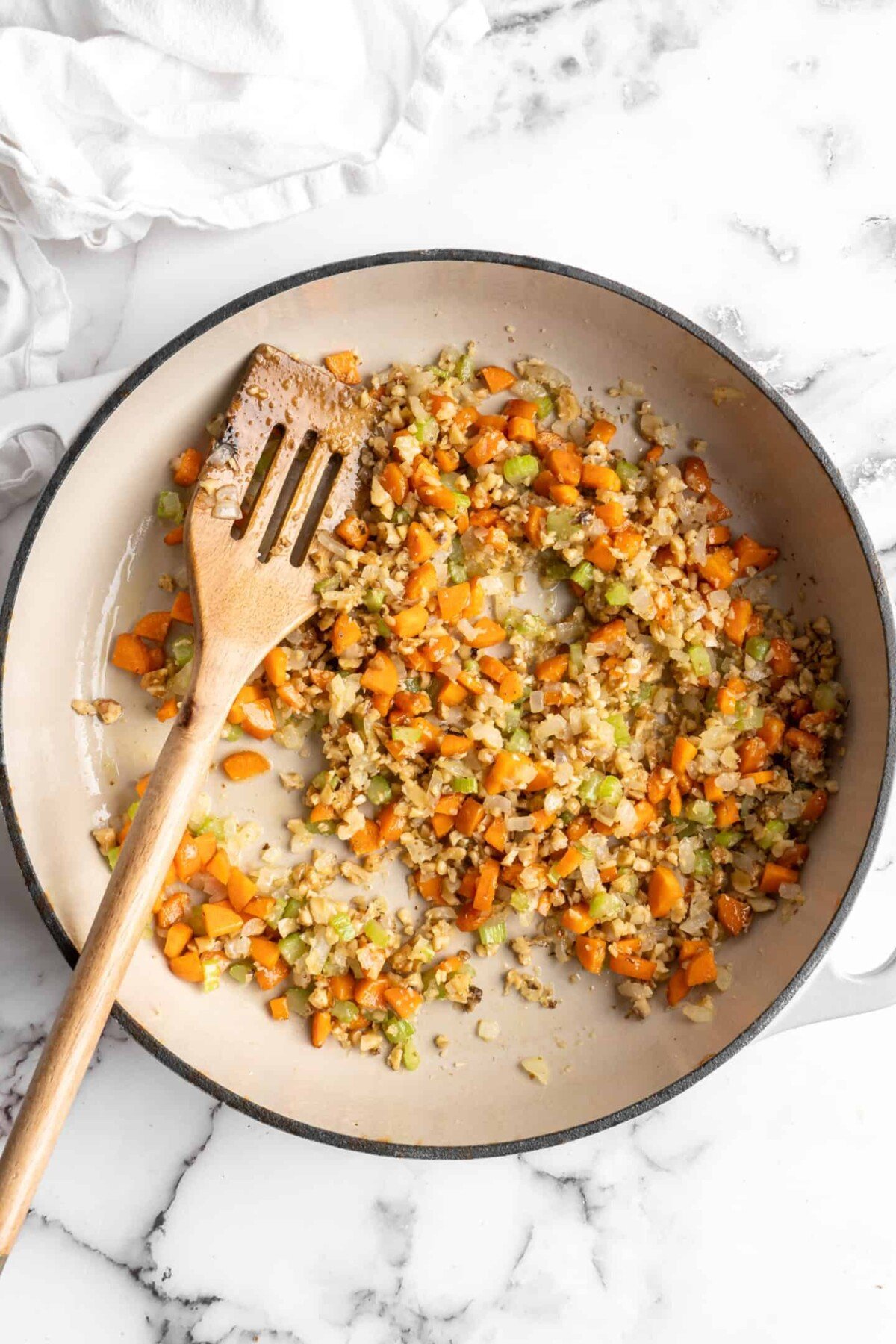 A pan with onions, carrots, celery, walnuts, and a wooden spoon in it