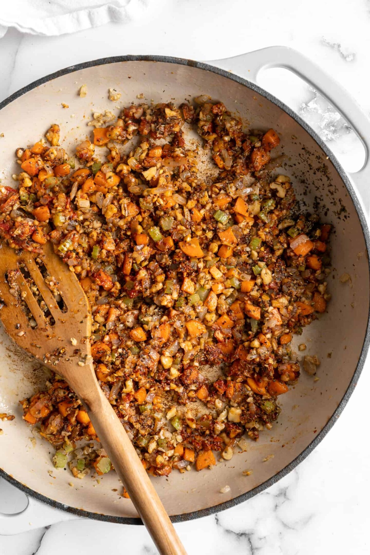 A pot with onions, carrots, celery, walnuts, garlic, tomato paste, and seasonings, with a wooden spoon in it.