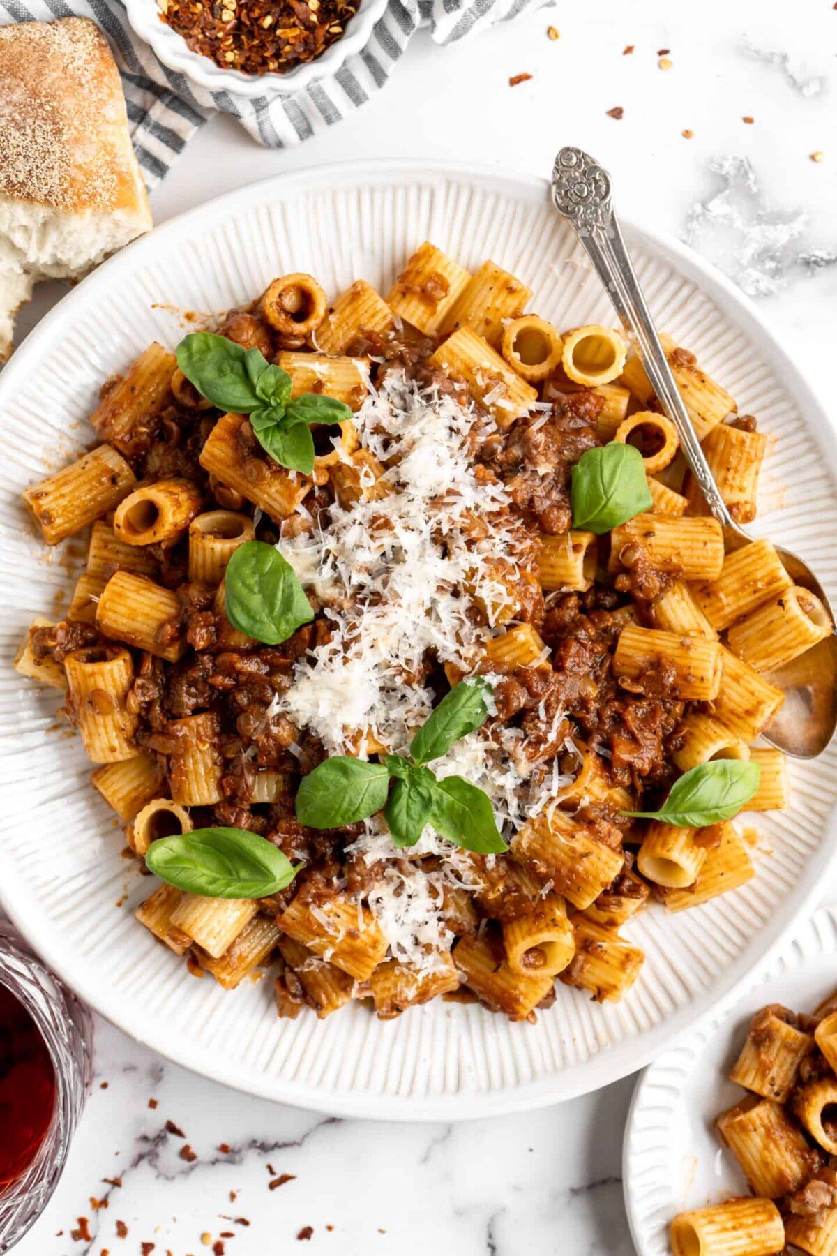 Overhead view of a plate of walnut lentil bolognese, garnished with basil and vegan parmesan, with a fork on the plate.