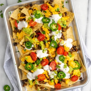 Overhead view of a tray of nachos covered in vegan sour cream, tomatoes, and jalapeños