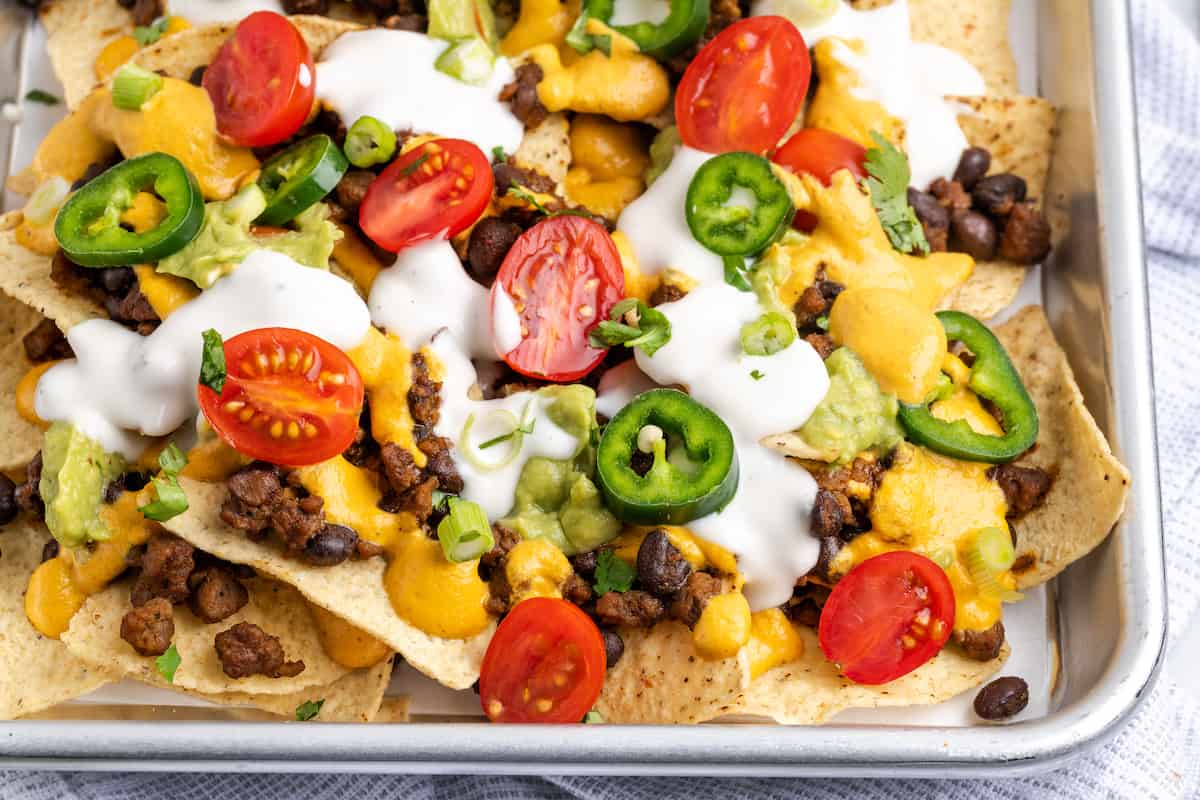 Close up of loaded vegan nachos covered in tomatoes, jalapeños, and vegan sour cream