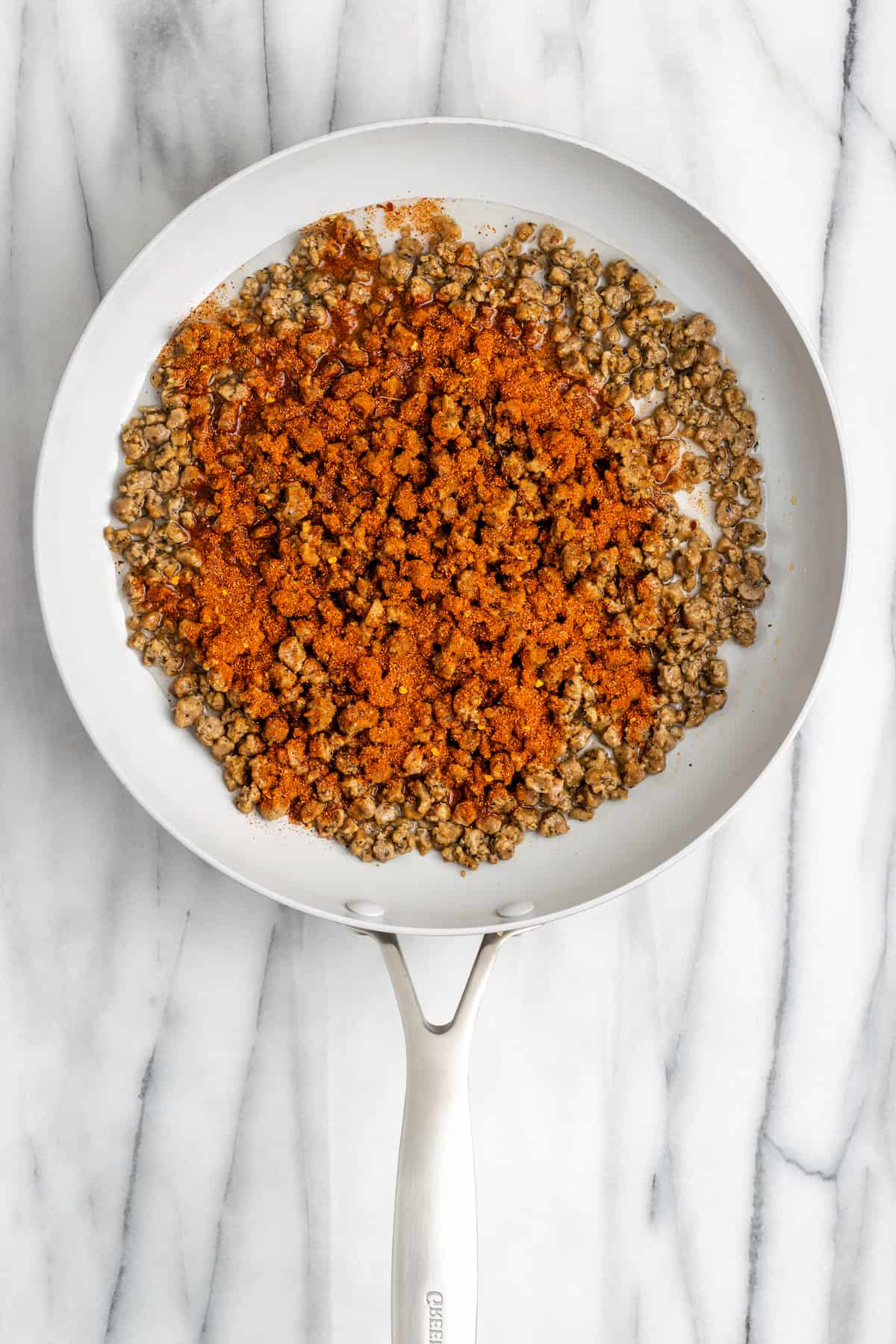 Vegan meat crumbles cooking in a pan, covered in taco seasoning