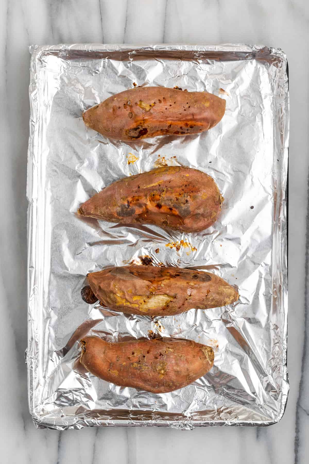 Four cooked sweet potatoes on an aluminum foil-lined baking sheet
