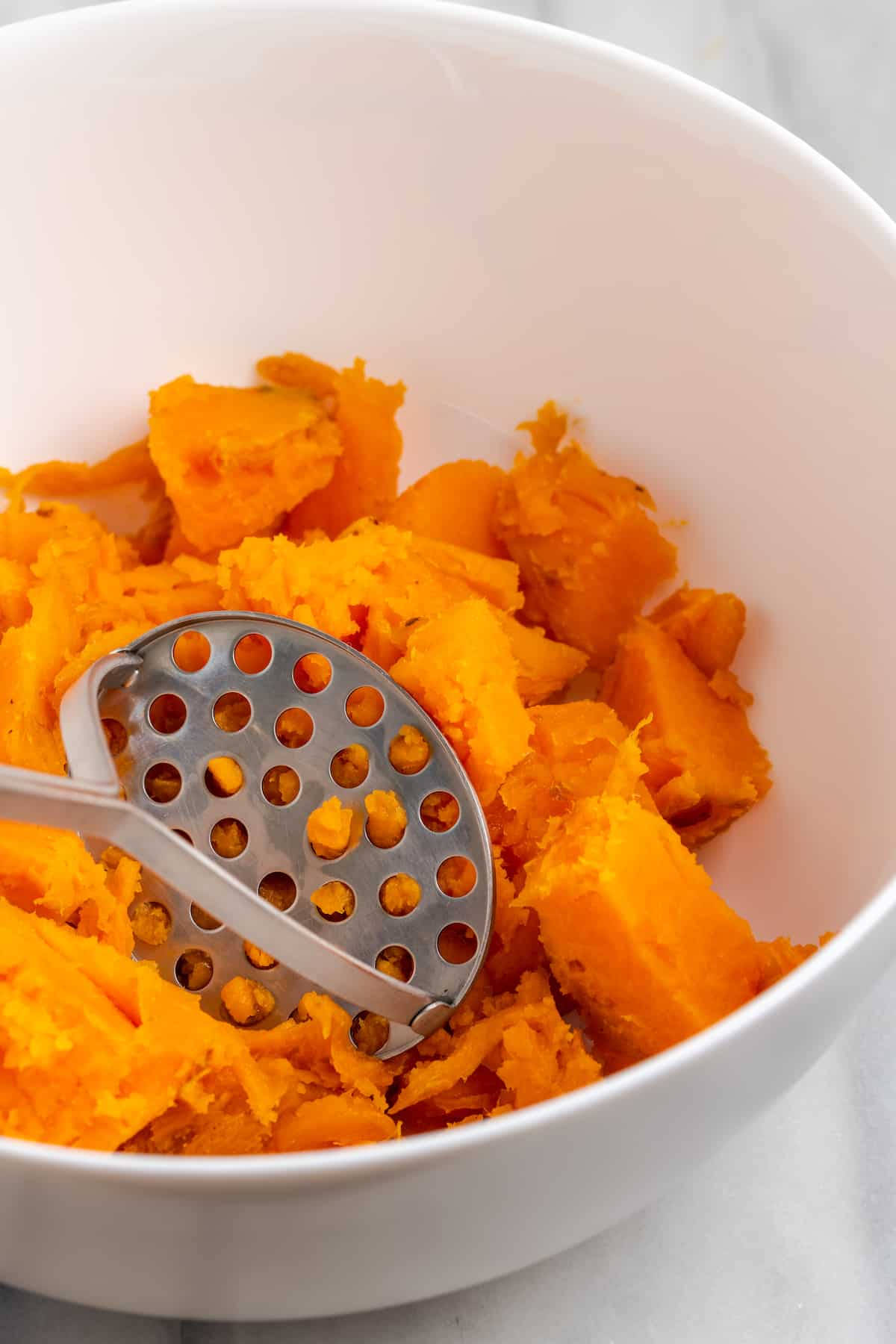 Close up of chunks of sweet potato in a mixing bowl with a potato masher
