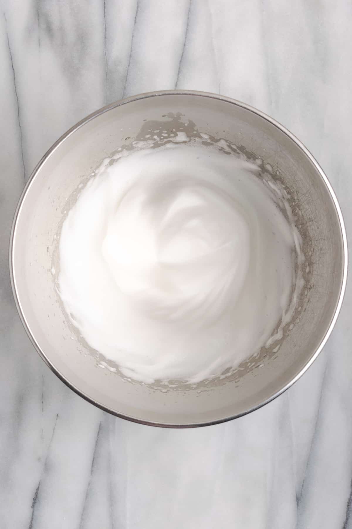 A mixing bowl filled with aquafaba whipped to stiff peaks.