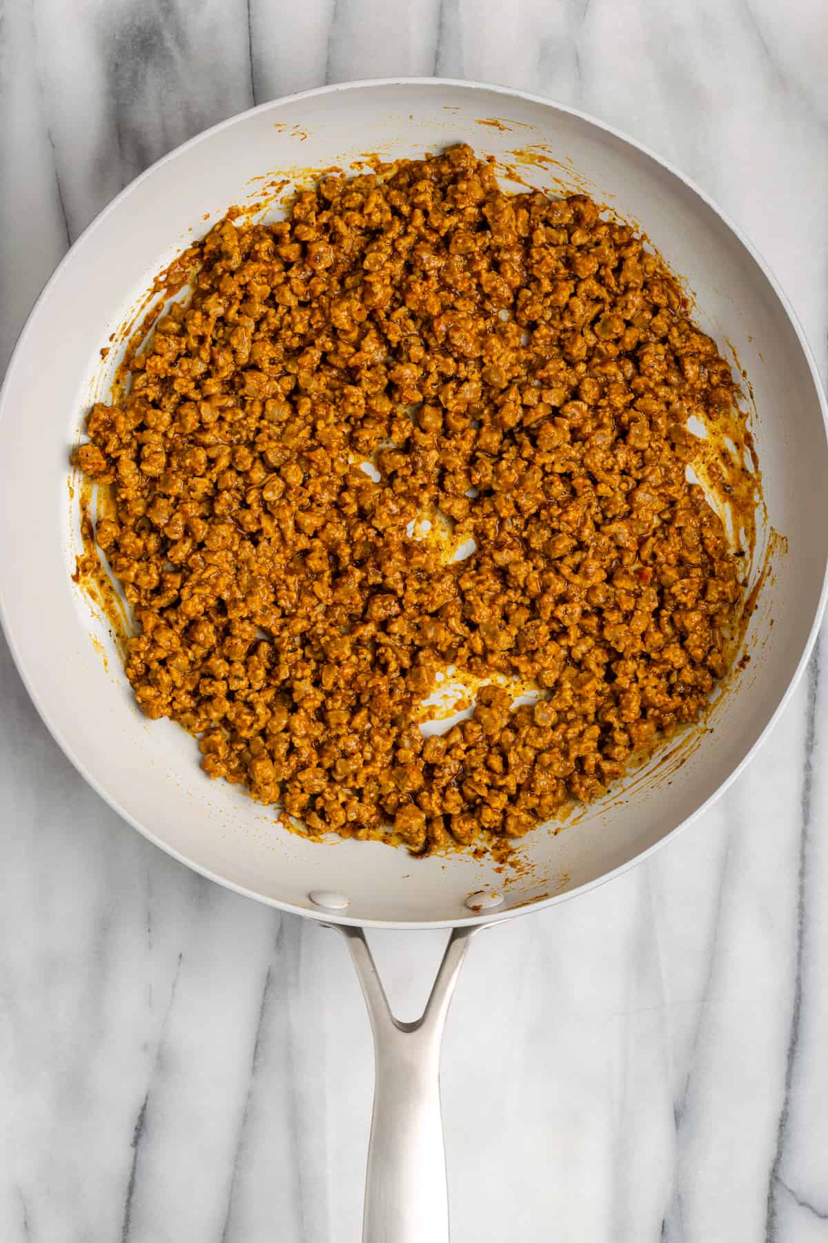 Vegan meat crumbles cooking in a pan with taco seasoning and water