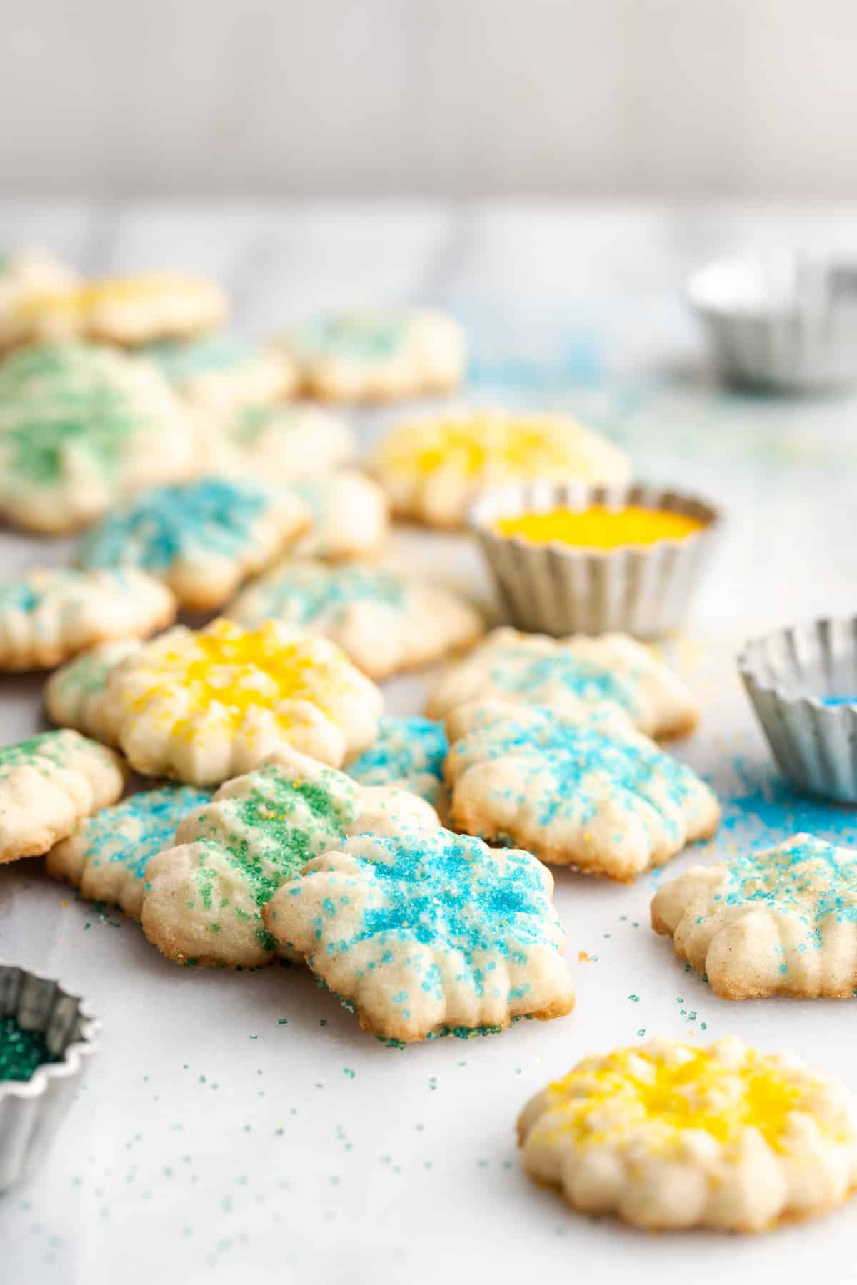 Lots of spritz cookies covered in sprinkles, next to a bowl of yellow sprinkles