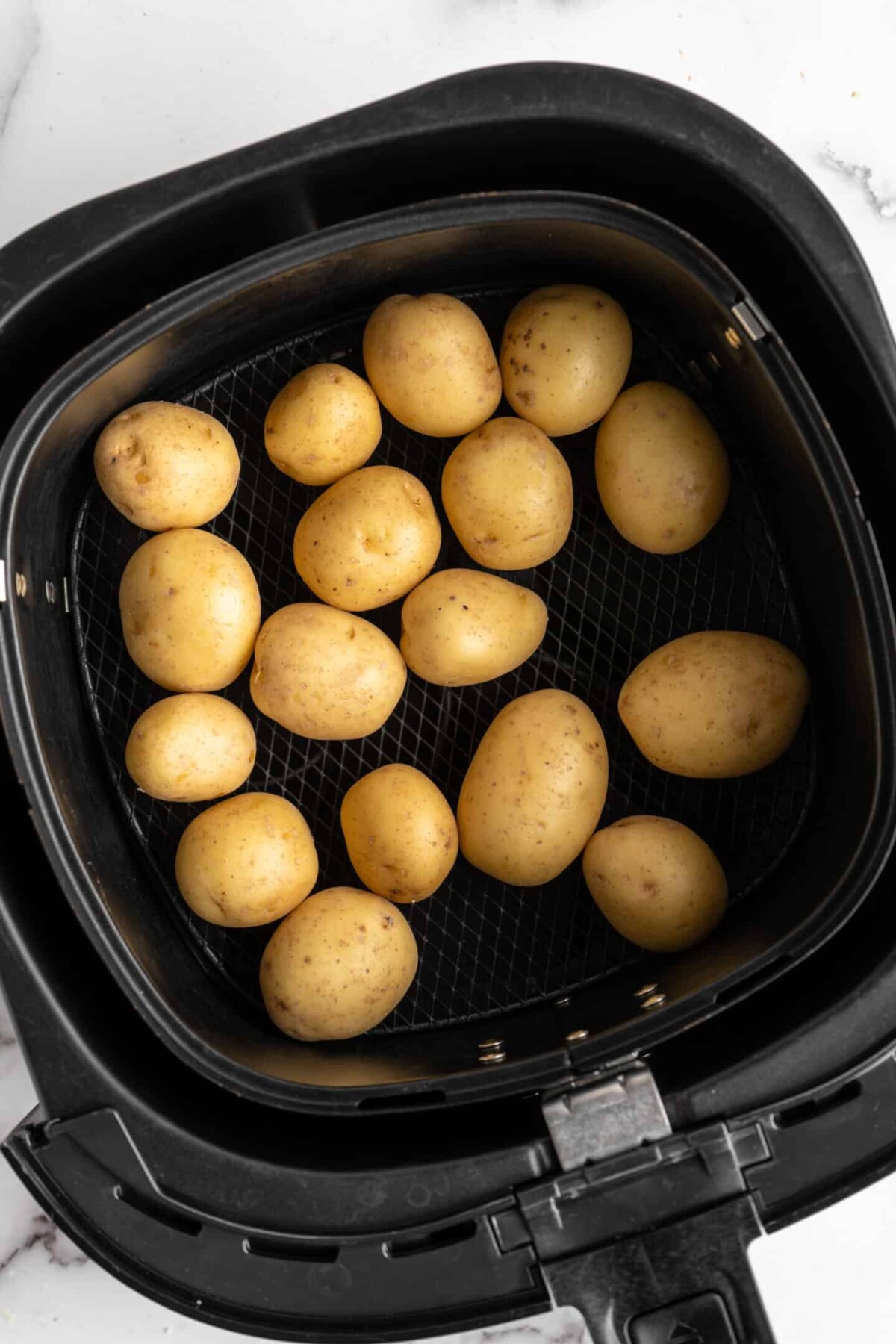 Uncooked baby potatoes in an air fryer basket