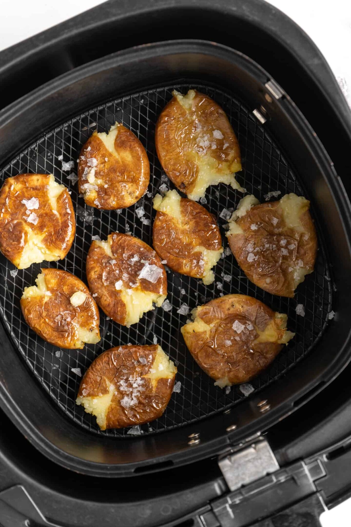 Smashed potatoes in an air fryer basket, topped with flaky salt, before being cooked a final time