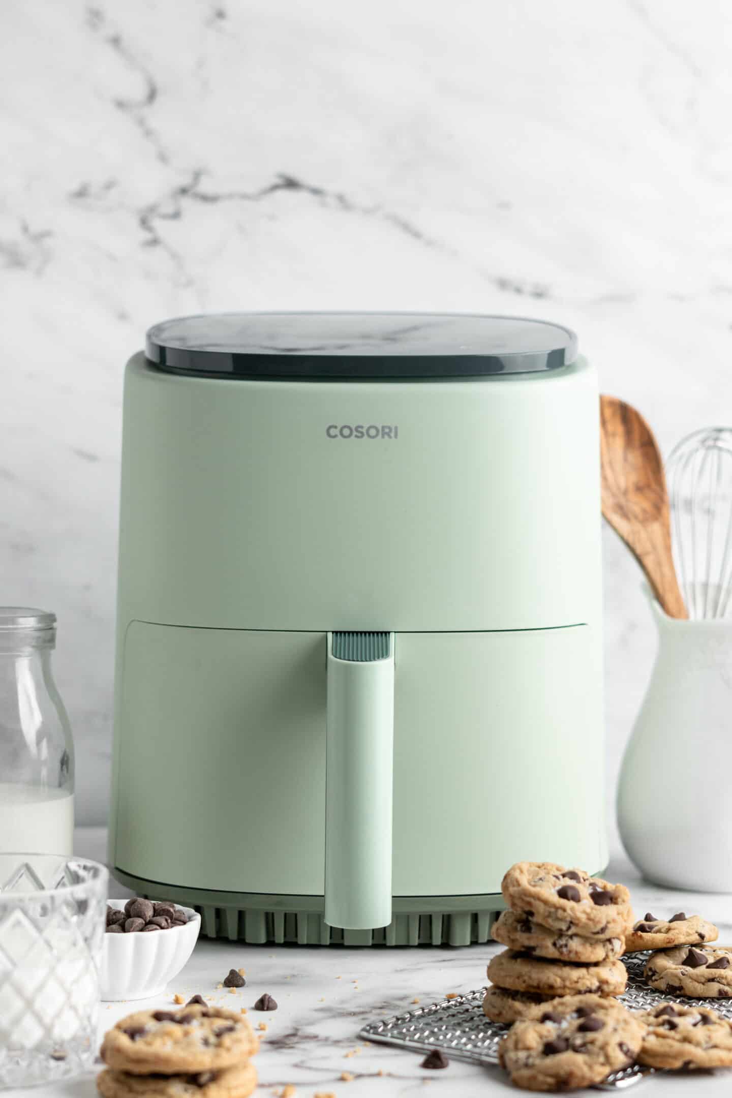 teal coloured air fryer with cookies stacked in front of it