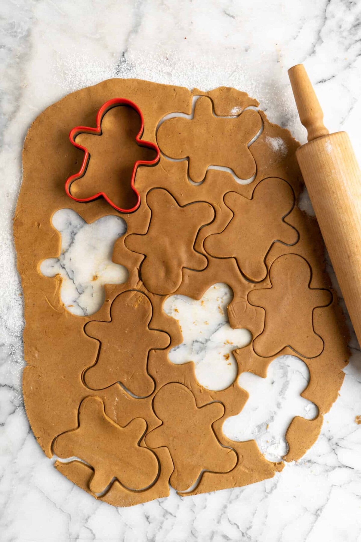 Rolled out gingerbread men dough with marks for a lot of gingerbread men to be cut out, and three gingerbread men already cut out, with a cookie cutter on top, and a rolling pin to the side