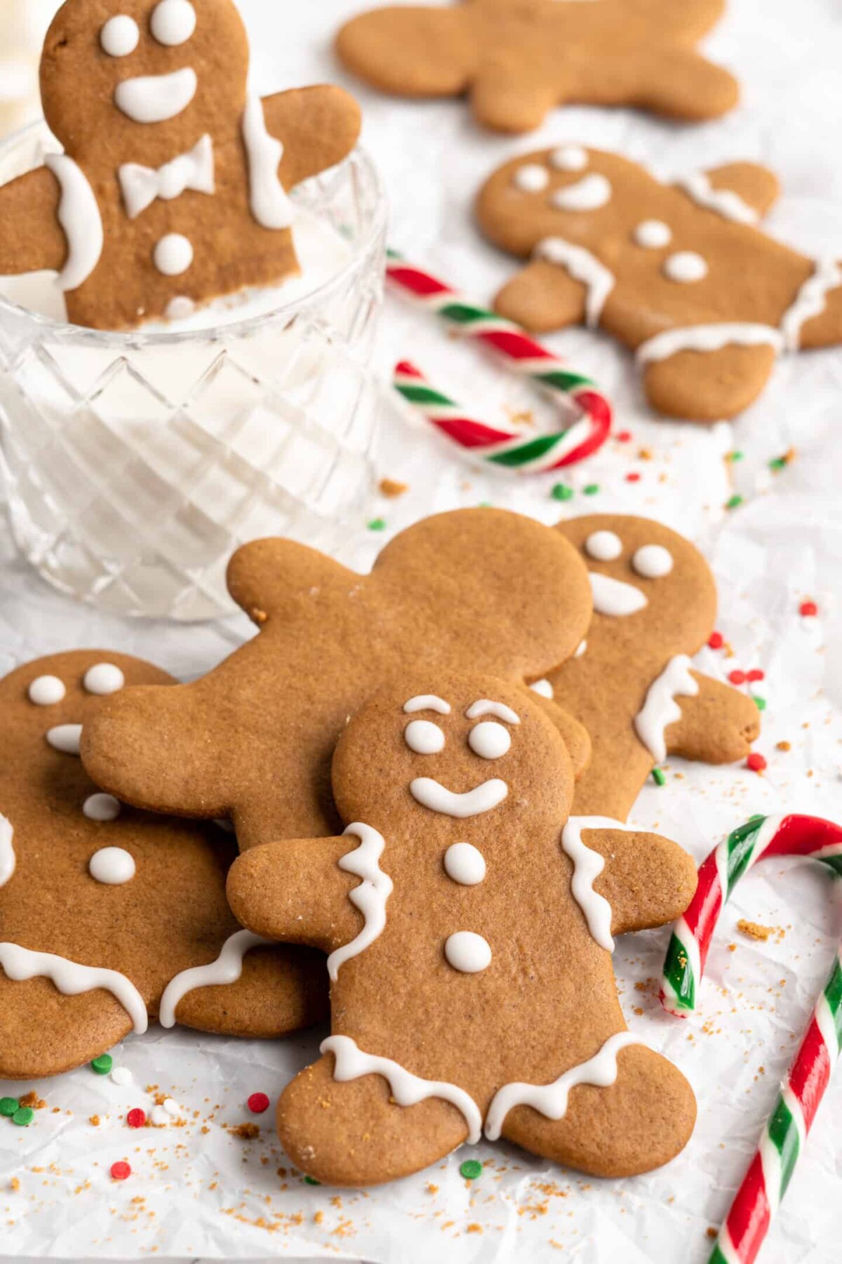 A pile of decorated gingerbread men cookies and one undecorated cookie, with candy canes around