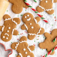A few decorated gingerbread men next to a few undecorated gingerbread men, surrounded by candy canes and a rolling pin