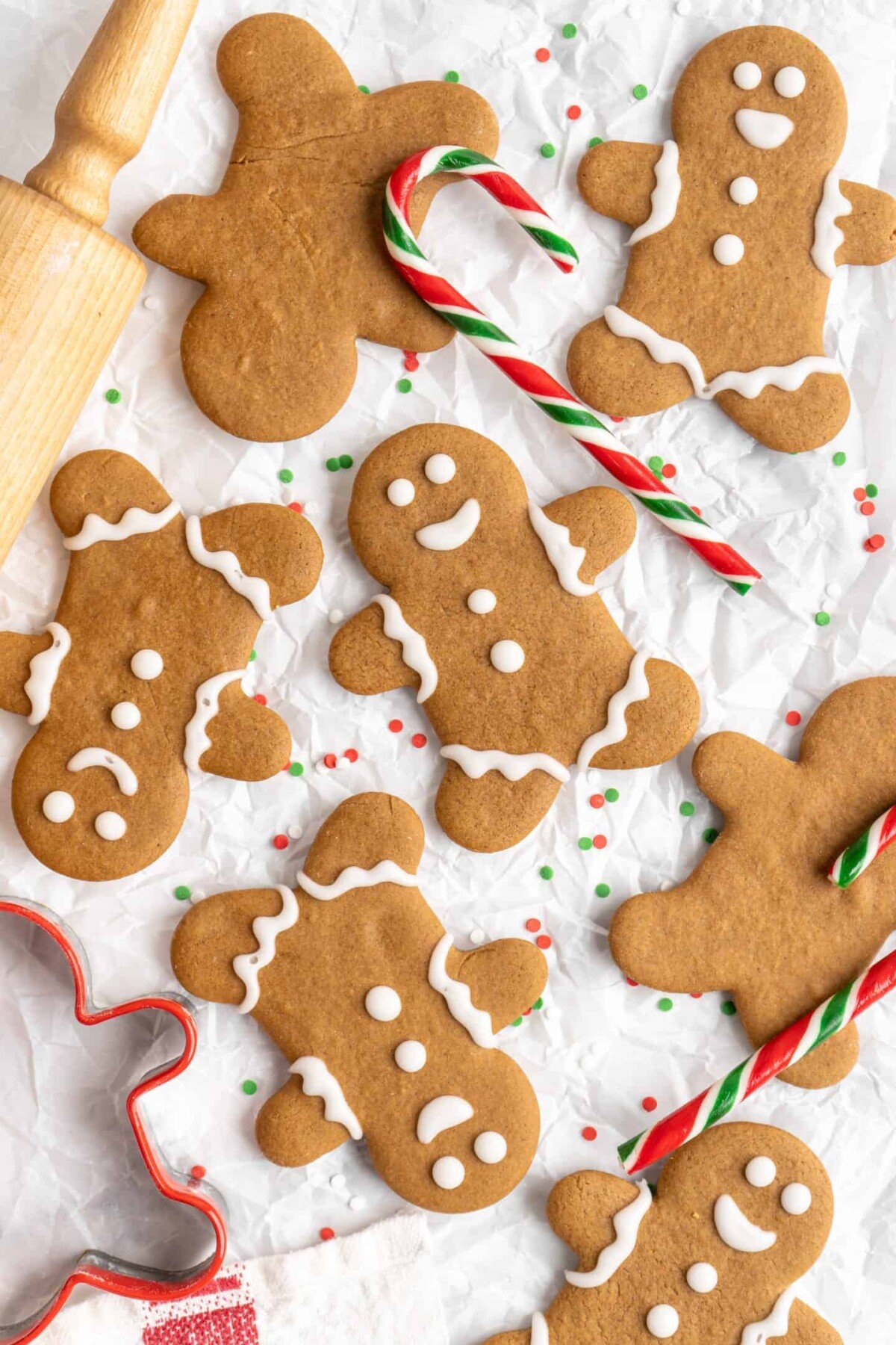 A few decorated gingerbread men next to a few undecorated gingerbread men, surrounded by candy canes and a rolling pin