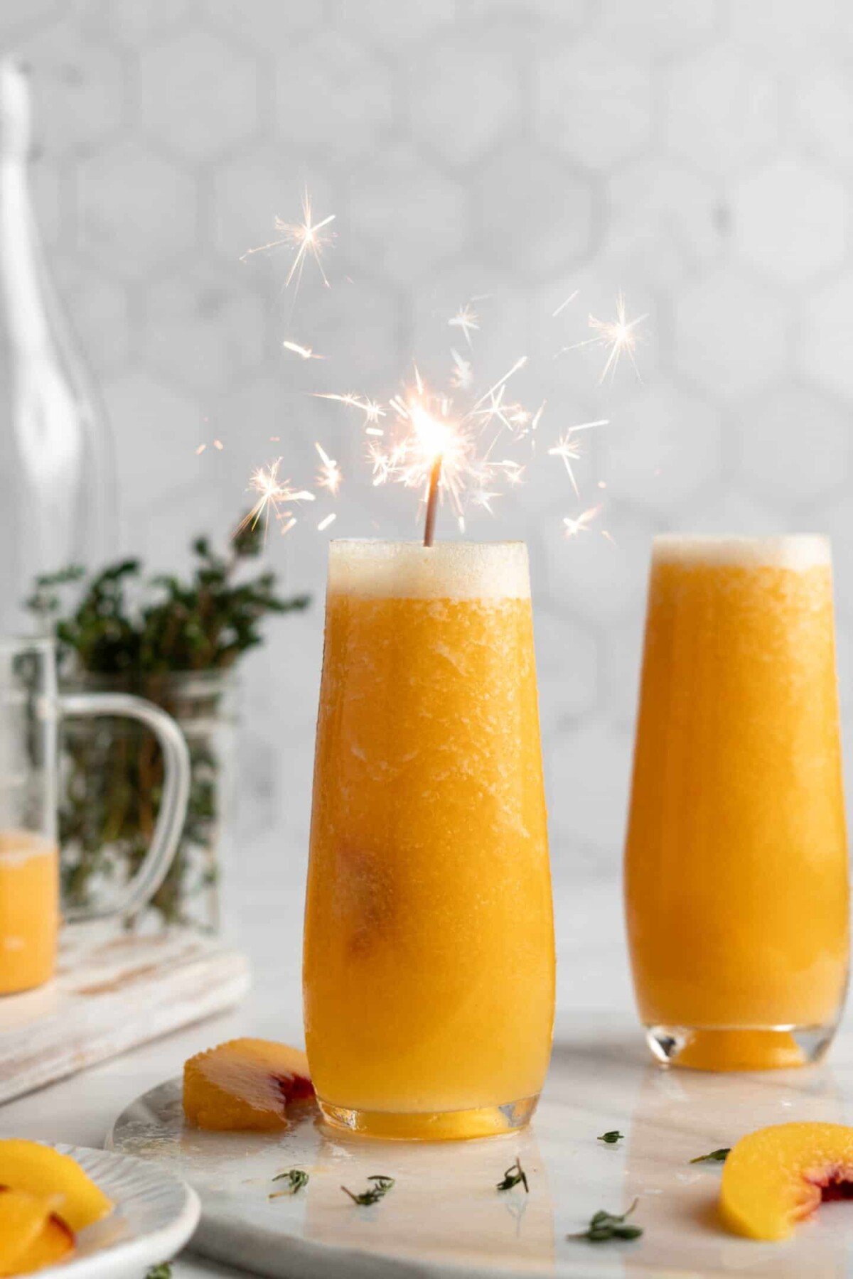 A peach bellini with a lit sparkler in it, next to another bellini