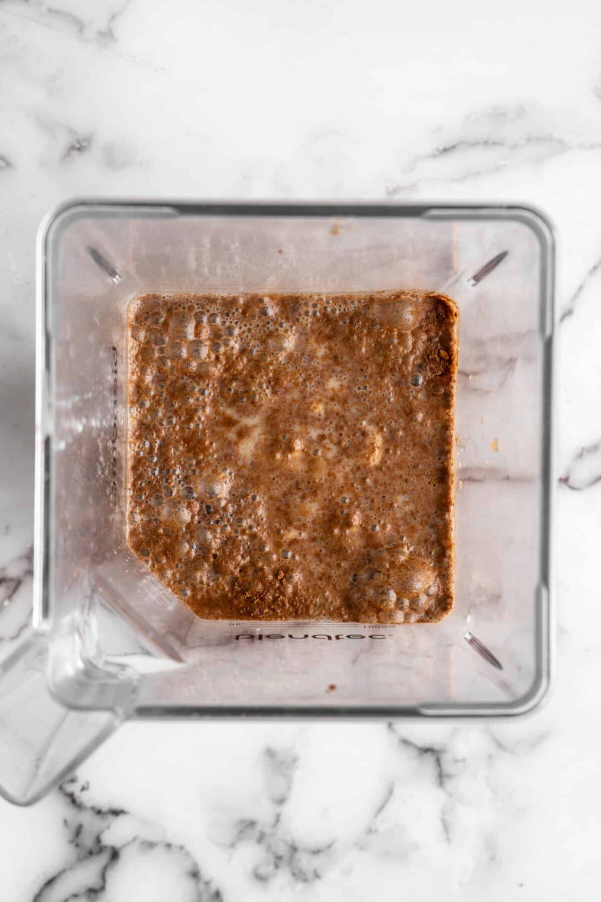 Overhead view of a blender filled with the ingredients for vegan eggnog, unblended, with cinnamon and pumpkin spice resting on the top