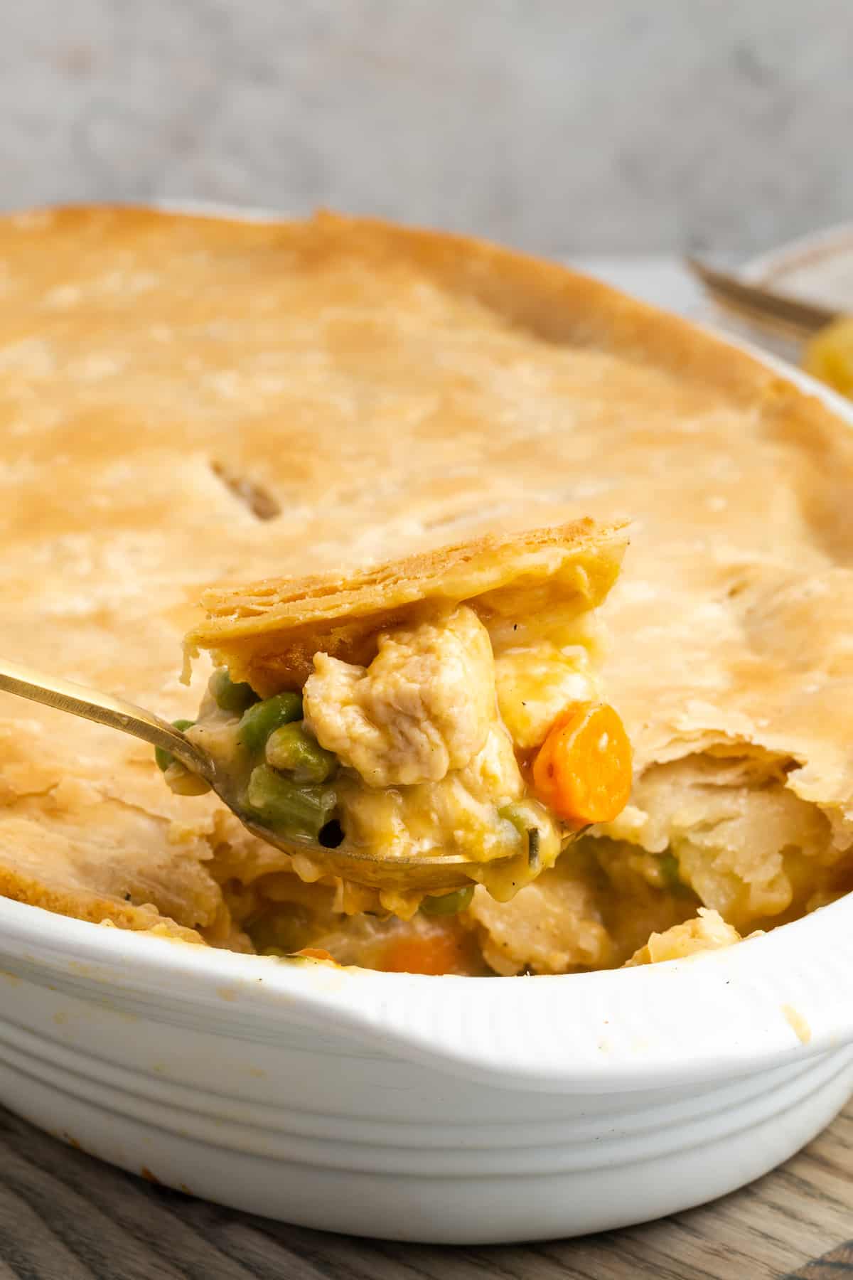 Close up of a spoonful of pot pie with a pot pie casserole in the background