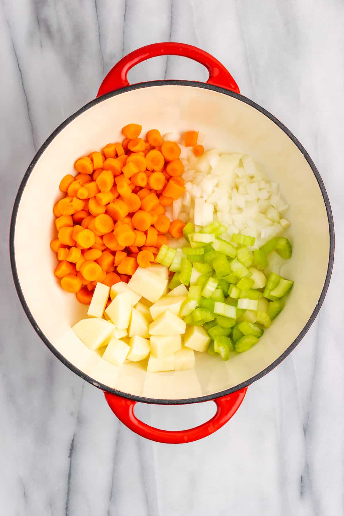 Dutch oven with raw carrots, potatoes, celery, and onions in it, divided into triangles