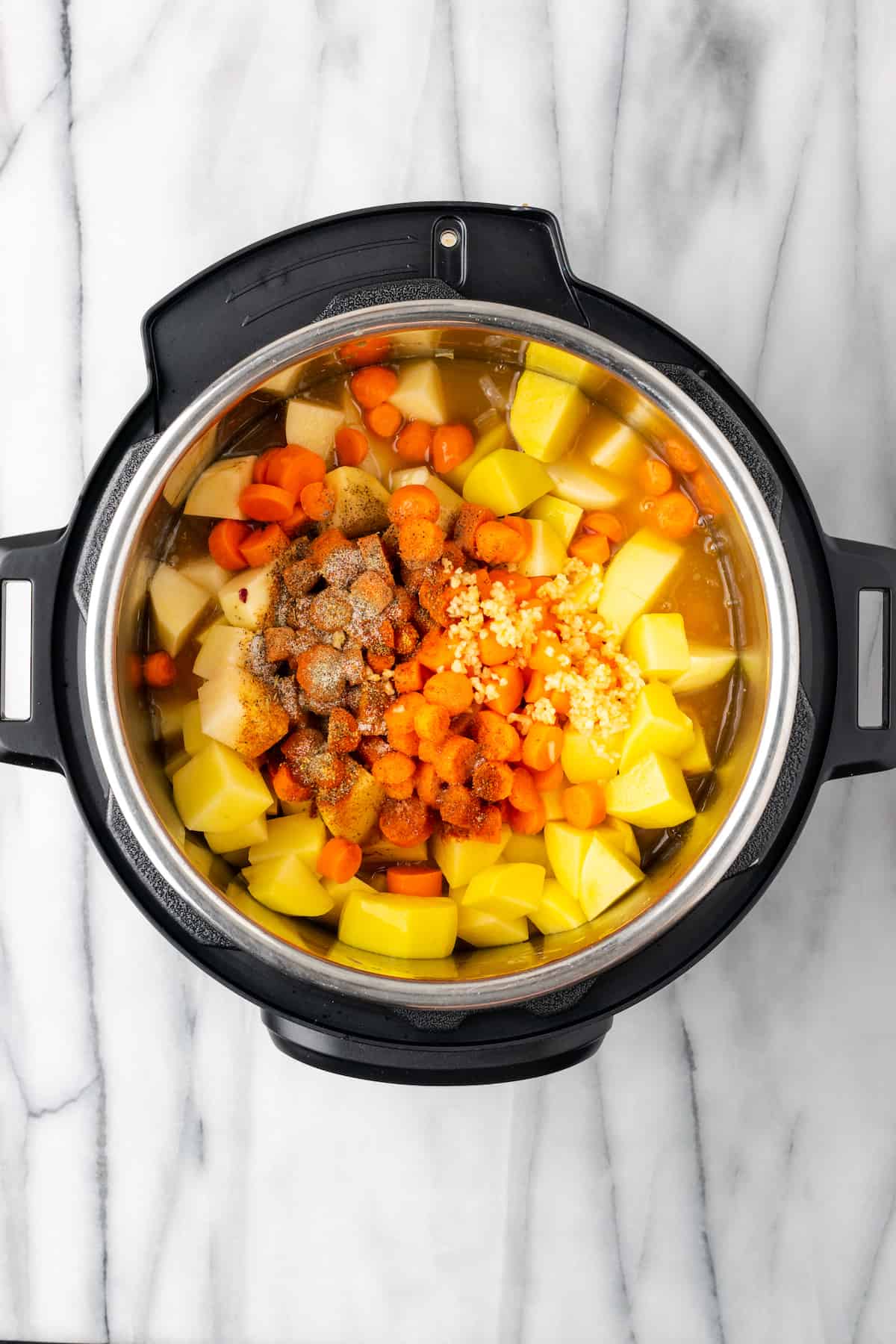 An instant pot filled with raw potatoes, carrot,s veggie broth, and seasonings