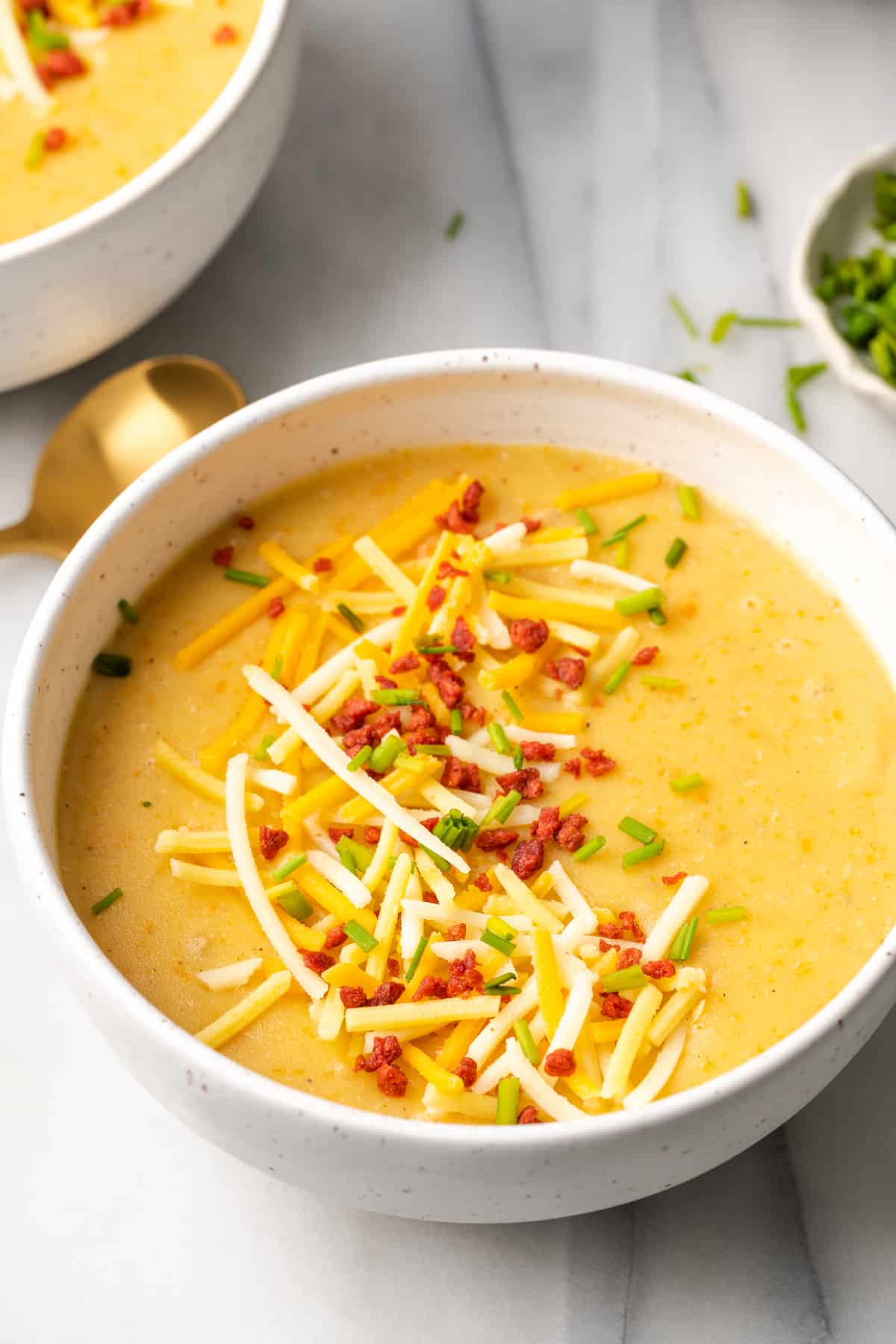 Close up of a bowl of potato soup garnished with vegan bacon bits, vegan cheese, and chives