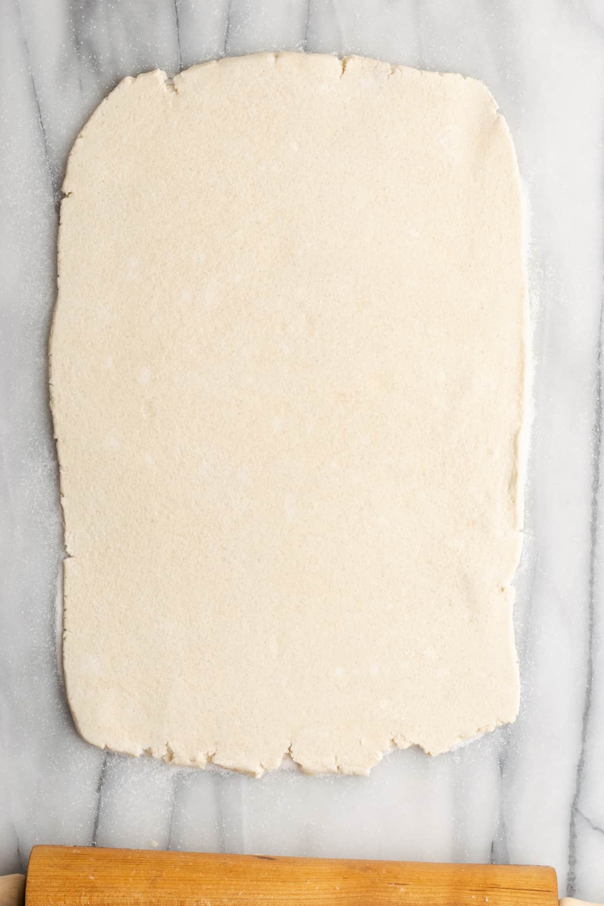 A rectangle of rolled out puff pastry with a rolling pin at the base