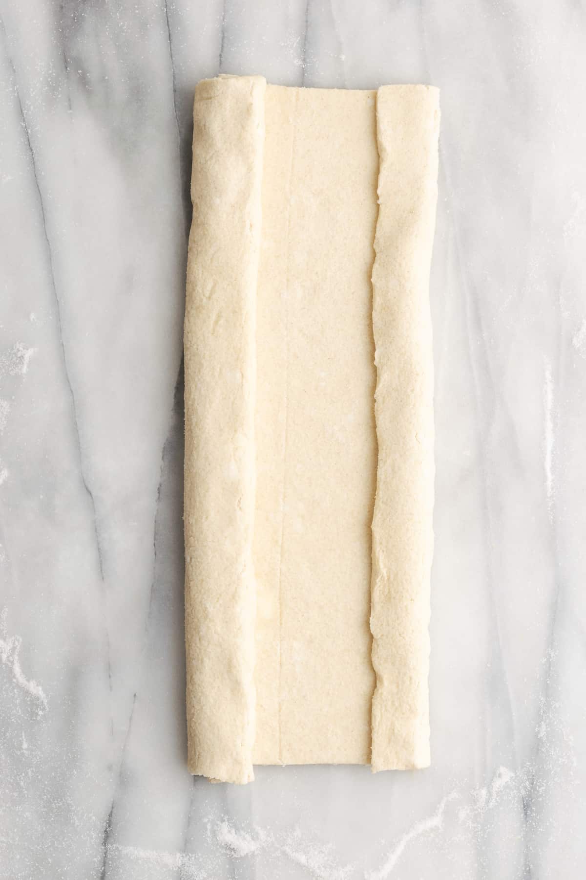 A rectangle of puff pastry dough with one side folded in about halfway, and the other about a quarter